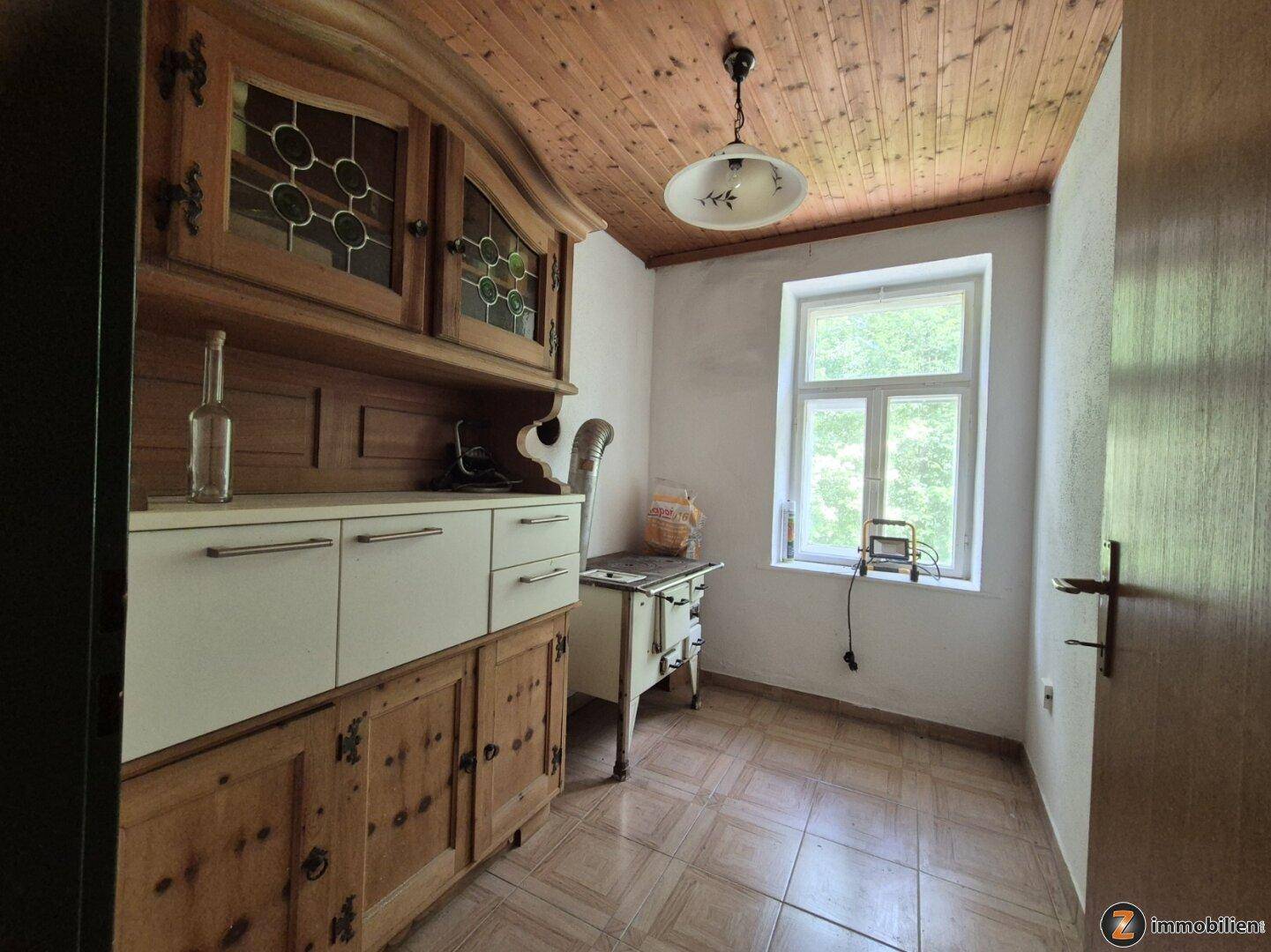 Traditionelle Küche mit Holzschrank, altem Ofen und Holzdecke, mit Blick ins Grüne.