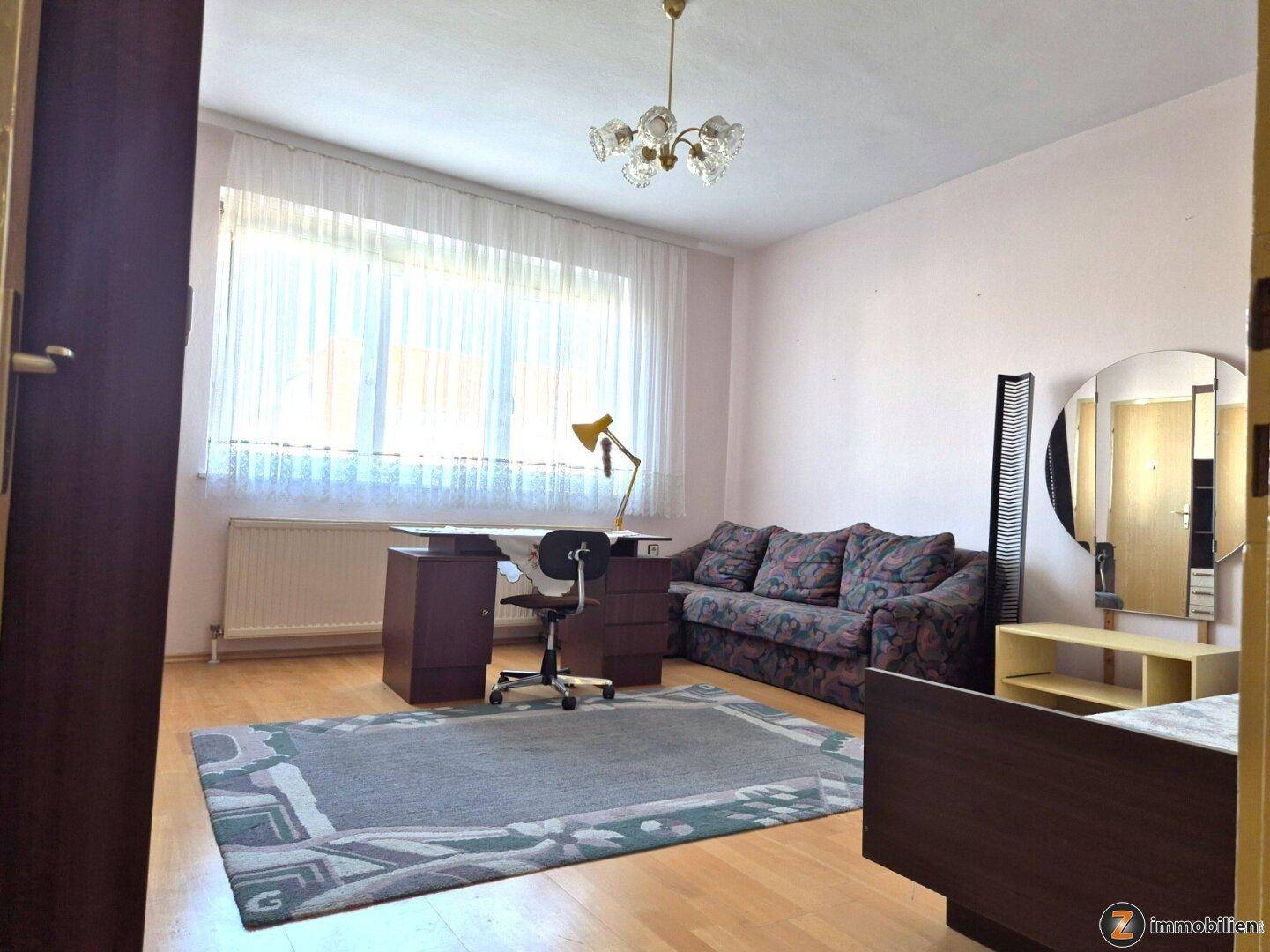 Geräumiges Zimmer mit Schreibtisch, Sofa und großem Fenster für viel Tageslicht.
