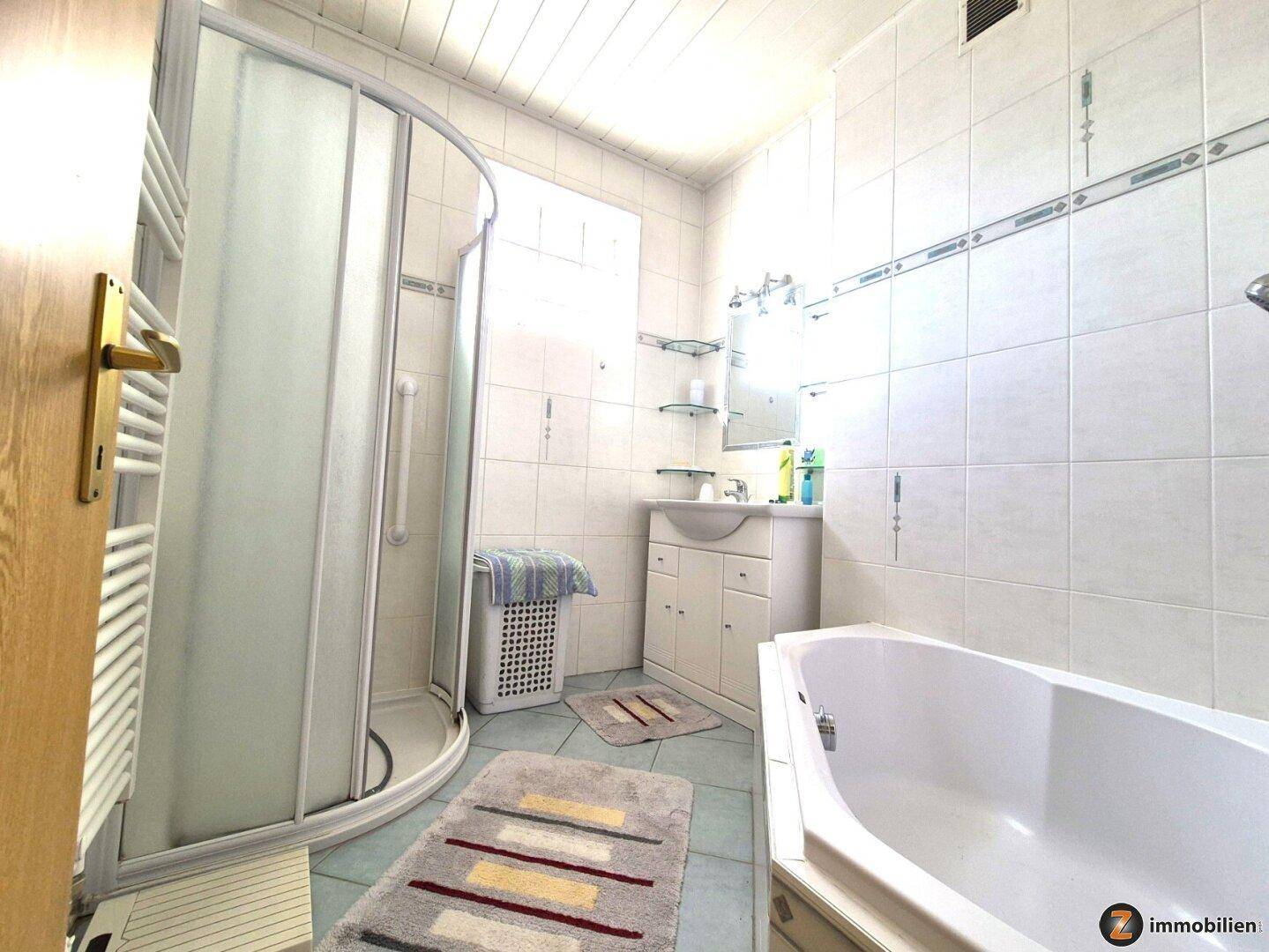 Badezimmer mit Dusche, Badewanne, Waschbecken und weiß gefliesten Wänden.