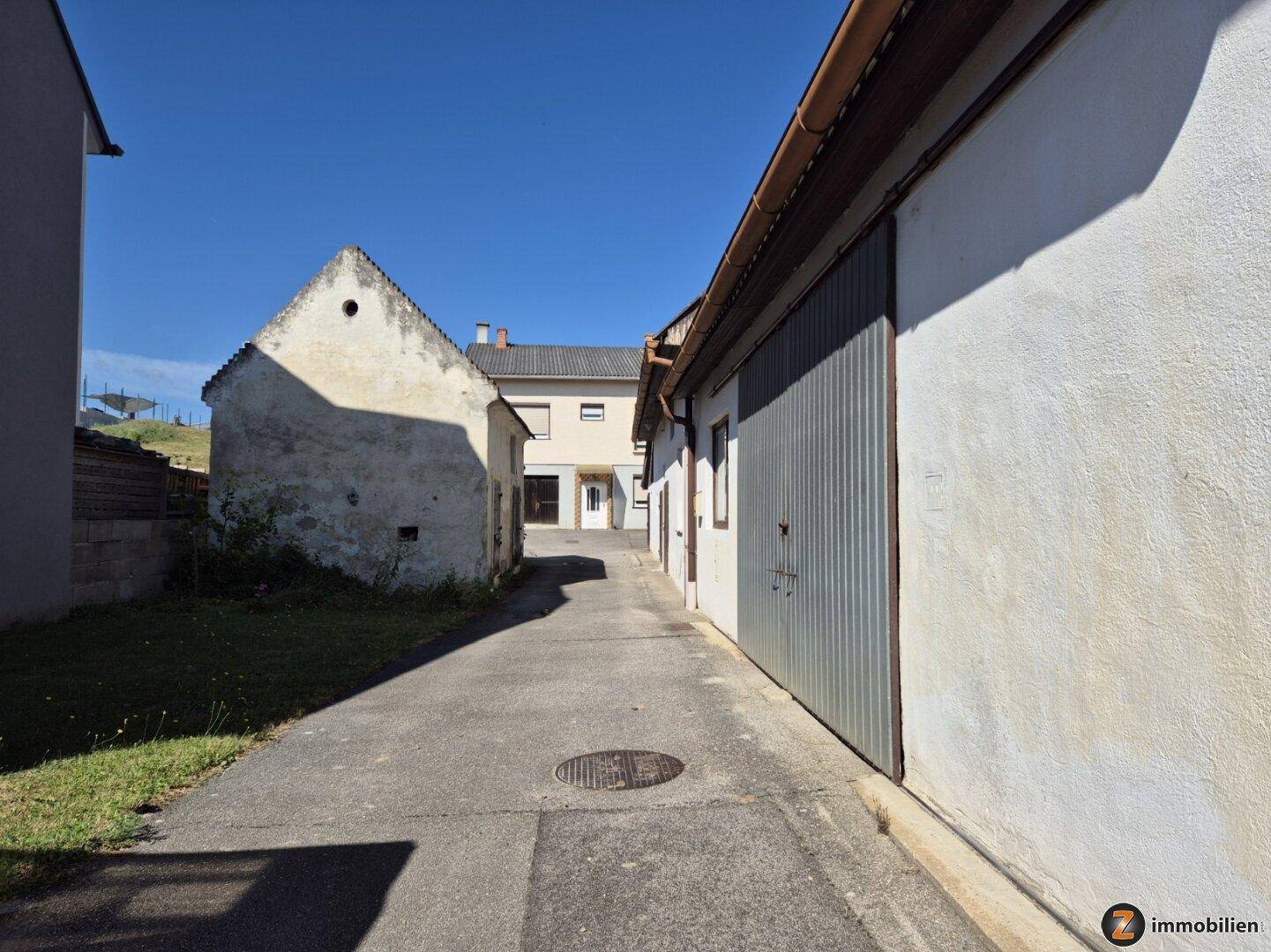 Zufahrt zwischen zwei Gebäuden, eines davon mit Garagentor und das andere ein älteres Haus.