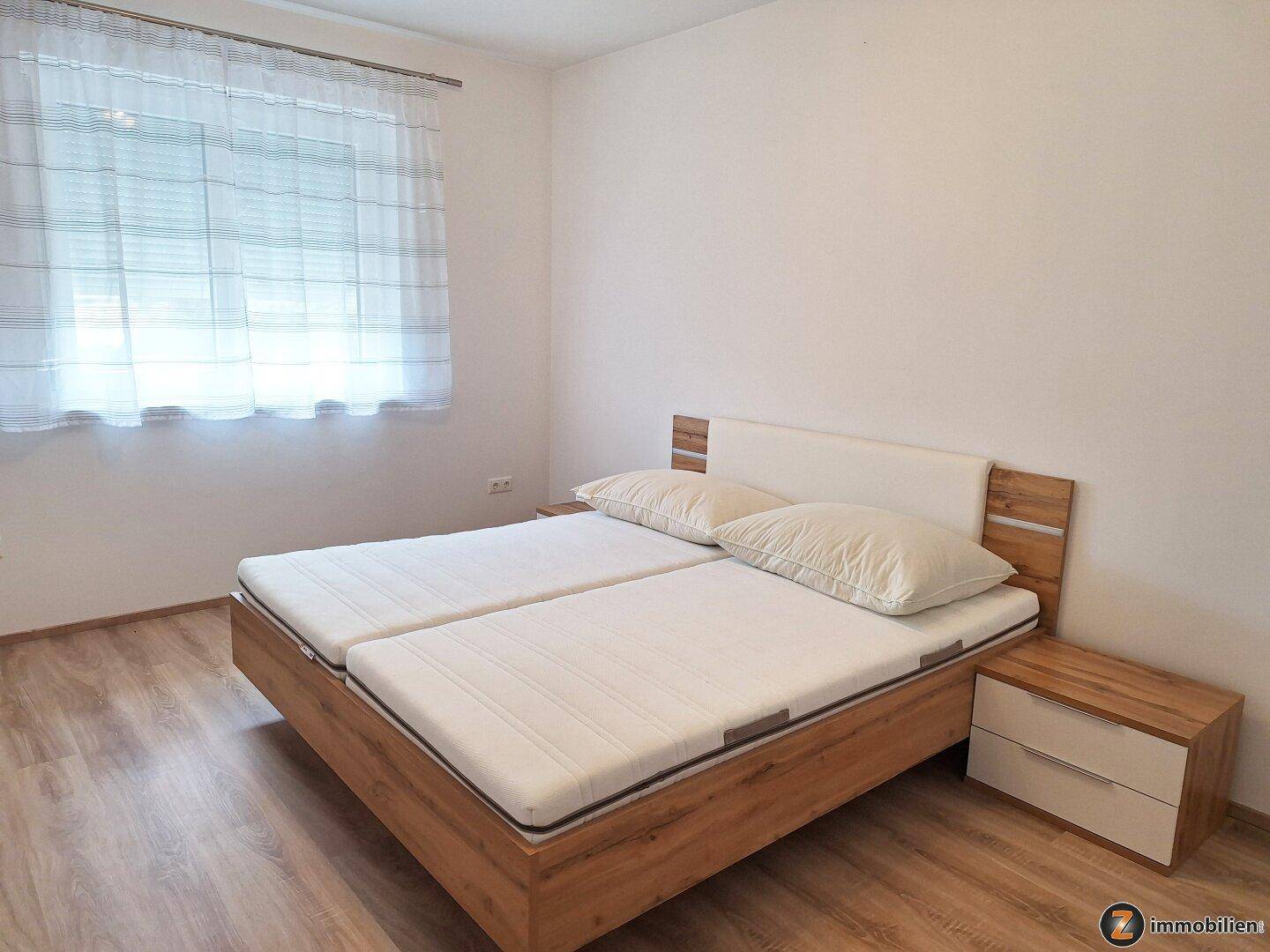 Freundliches Schlafzimmer mit zwei Einzelbetten, Nachttischen und Holzoptikboden.