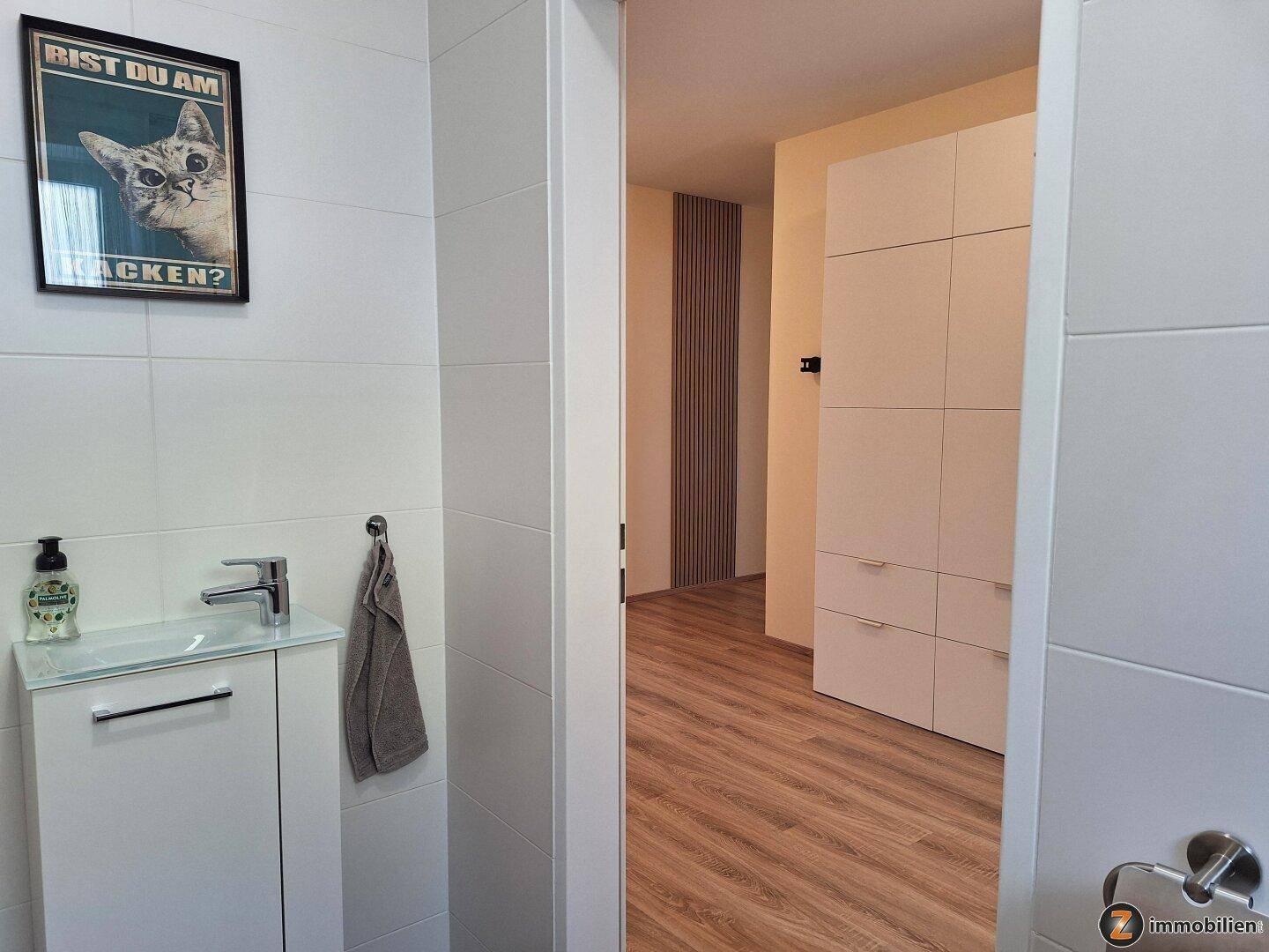 Kleines Gäste-WC mit Waschtisch, Spiegel und Zugang zum Flur.