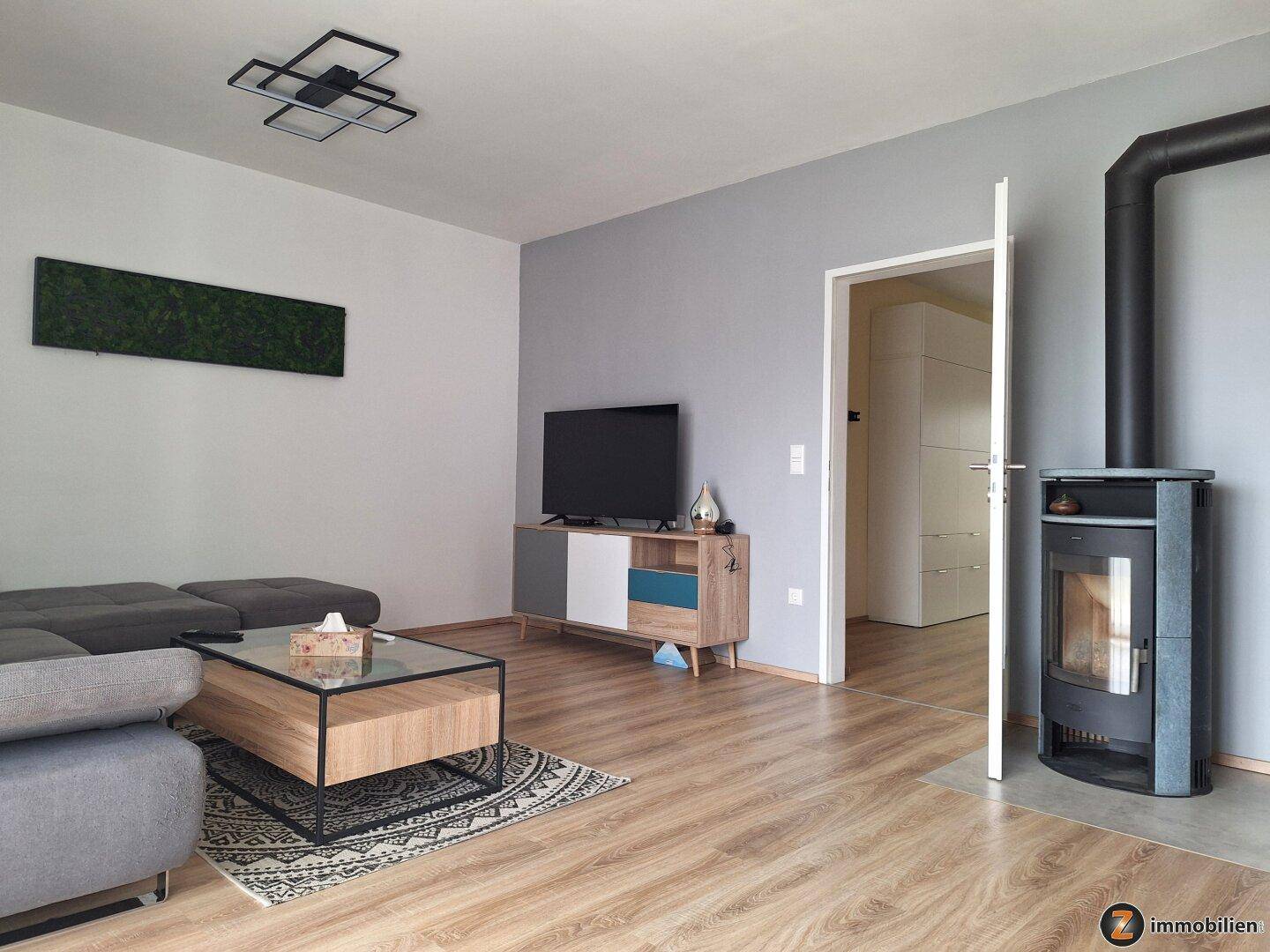 Gemütliches Wohnzimmer mit Kaminofen, Sofa, TV-Möbel und Holzoptikboden.