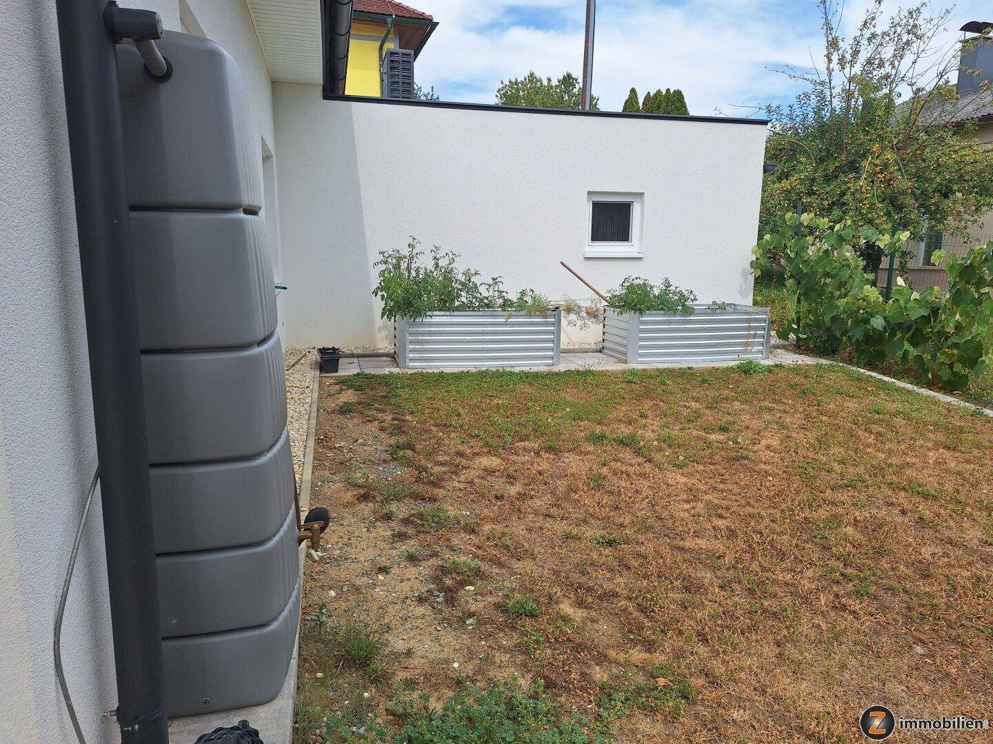 Kleiner Gartenbereich mit Hochbeeten für Gemüseanbau und Regentonne.