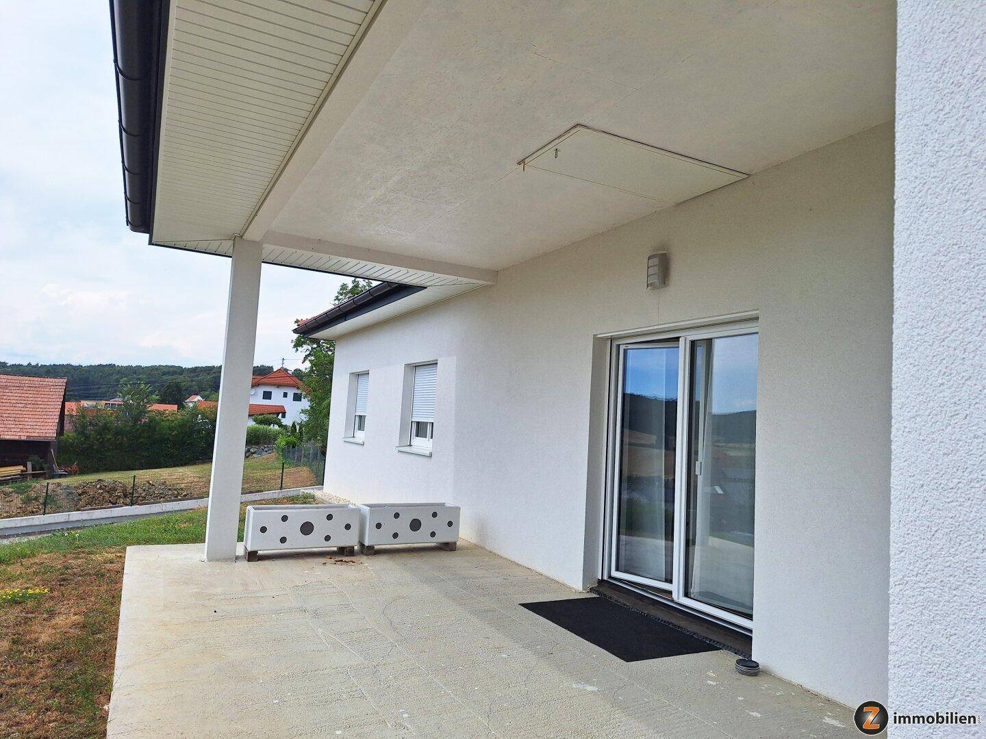 Überdachte Terrasse mit Schiebetüren zum Wohnbereich und Blick ins Grüne.