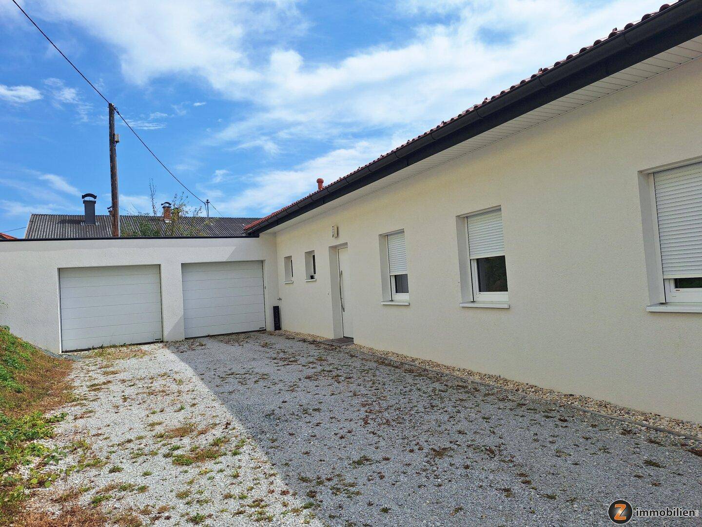 Seitenansicht des Hauses mit Kiesauffahrt und Doppelgarage unter blauem Himmel.