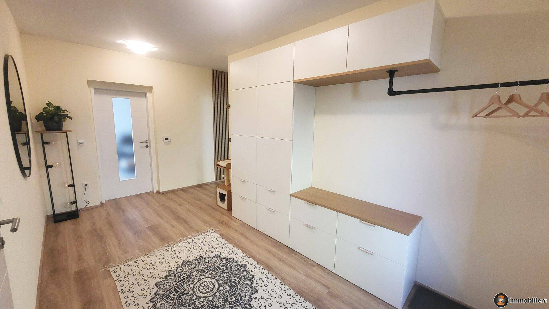 Geräumiger Flur mit weißem Garderobenschrank, Ablagefläche und Spiegel.