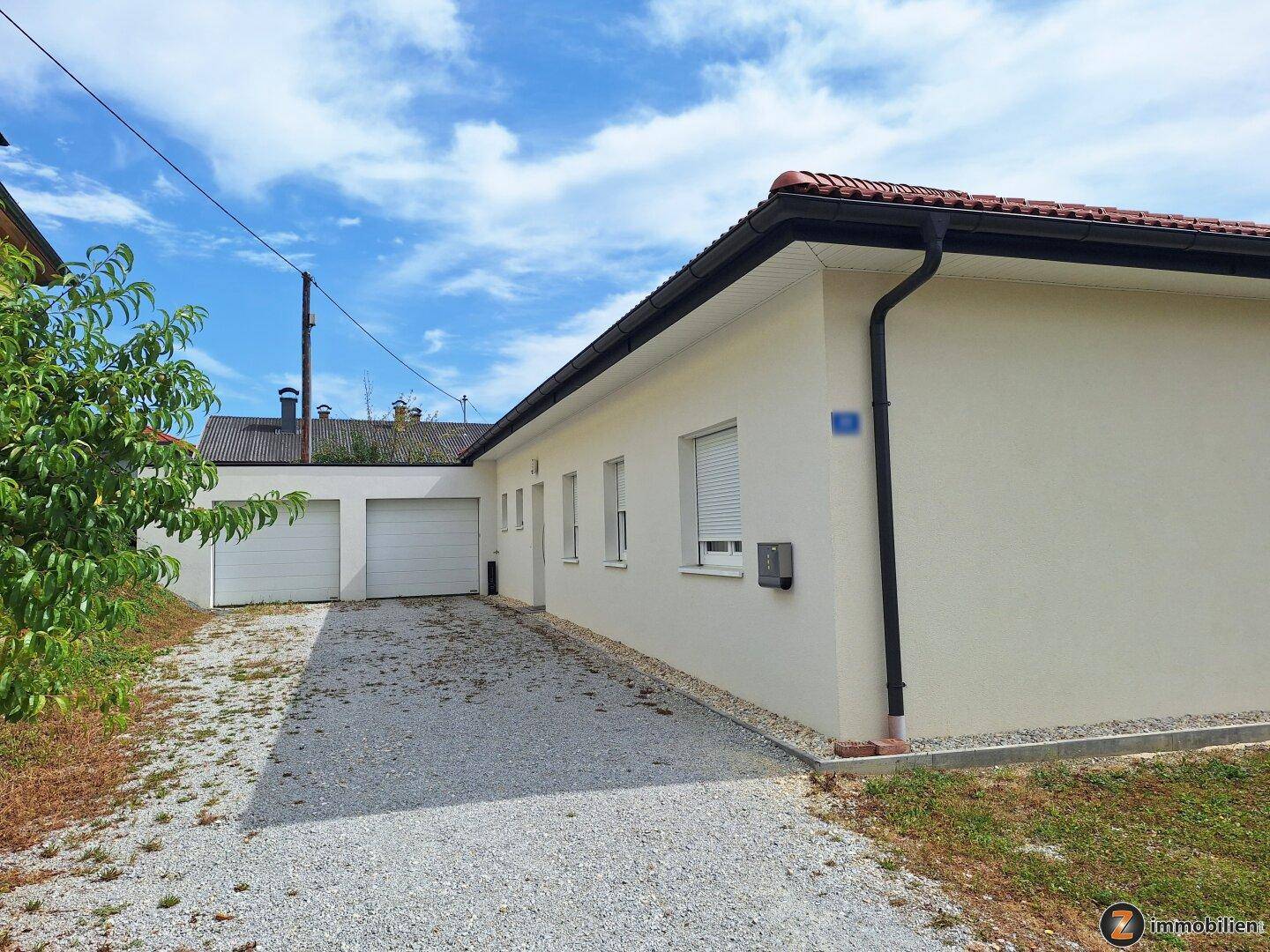 Seitenansicht des Hauses mit Kiesauffahrt und Doppelgarage unter blauem Himmel.