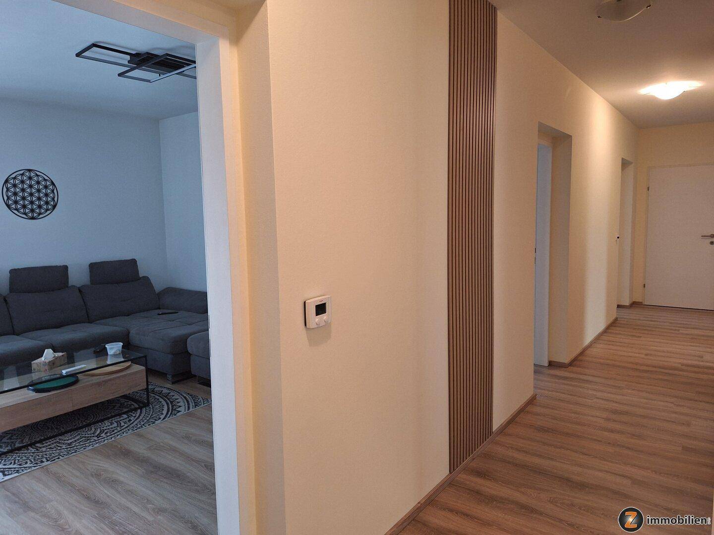 Heller Flur mit Laminatboden und modernem Wandakzent, der in ein Wohnzimmer führt.
