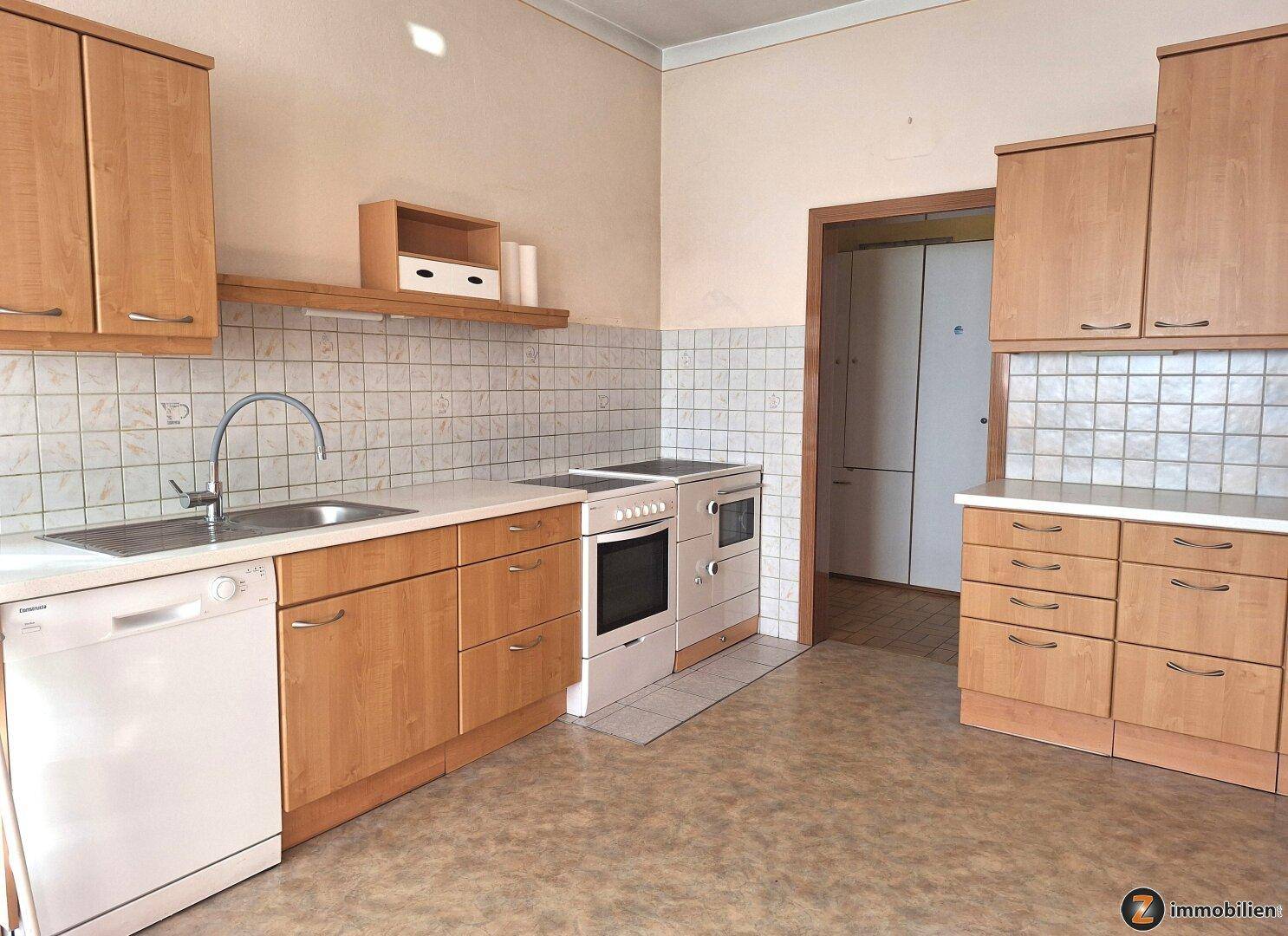 Funktionale Küche mit hellen Holzschränken, weißen Arbeitsplatten und Fliesenrückwand, inklusive Geschirrspüler.