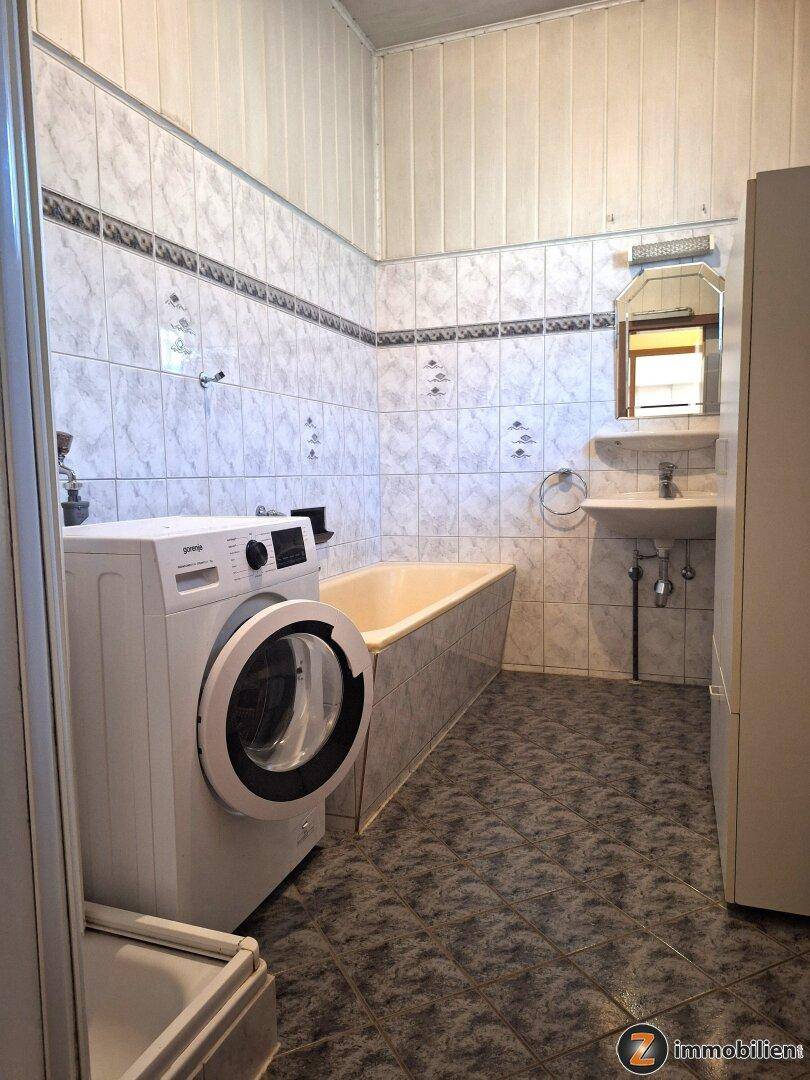 Badezimmer mit Badewanne, Waschbecken, Waschmaschine und gefliesten Wänden und Boden.