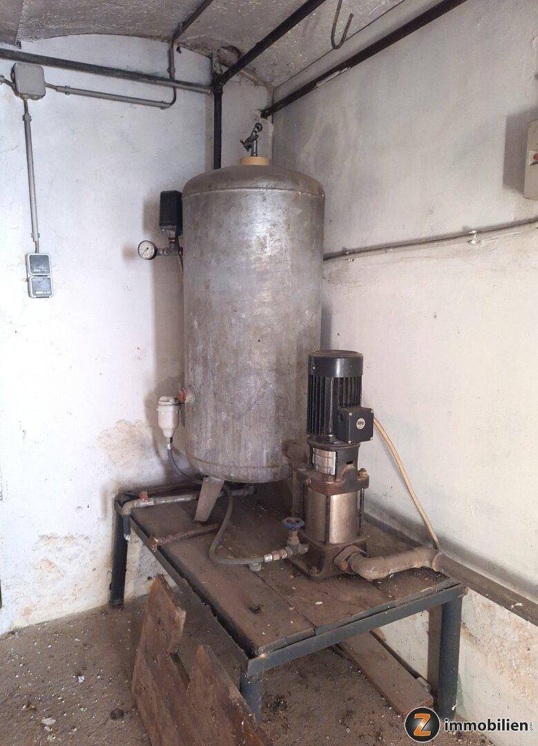 Kellerraum mit großem Metalltank und Pumpensystem, wahrscheinlich für die Wasserversorgung.