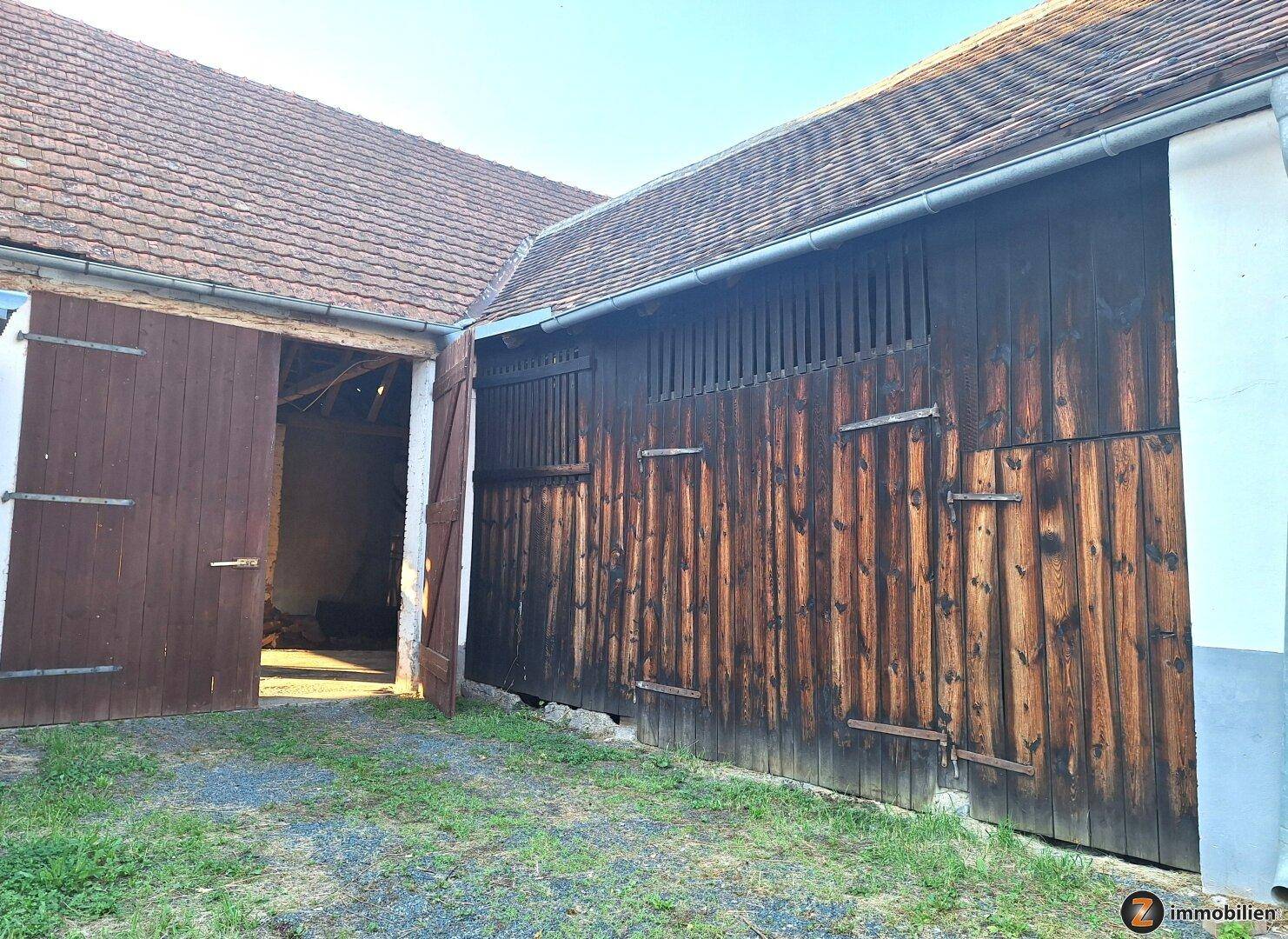 Außenansicht einer großen Holzscheune mit geöffneten Toren, die den Innenraum offenbaren.