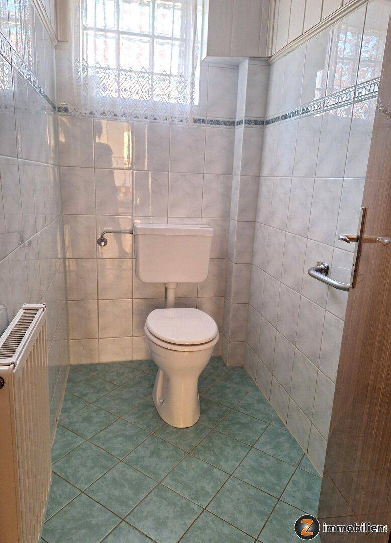Separates WC mit Toilette, Heizkörper und vollständig gefliesten Wänden und Boden.