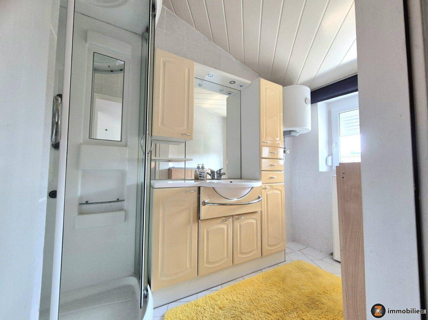 Helles Badezimmer mit Dusche, Waschtisch und Spiegelschrank unter einer Holzdecke.