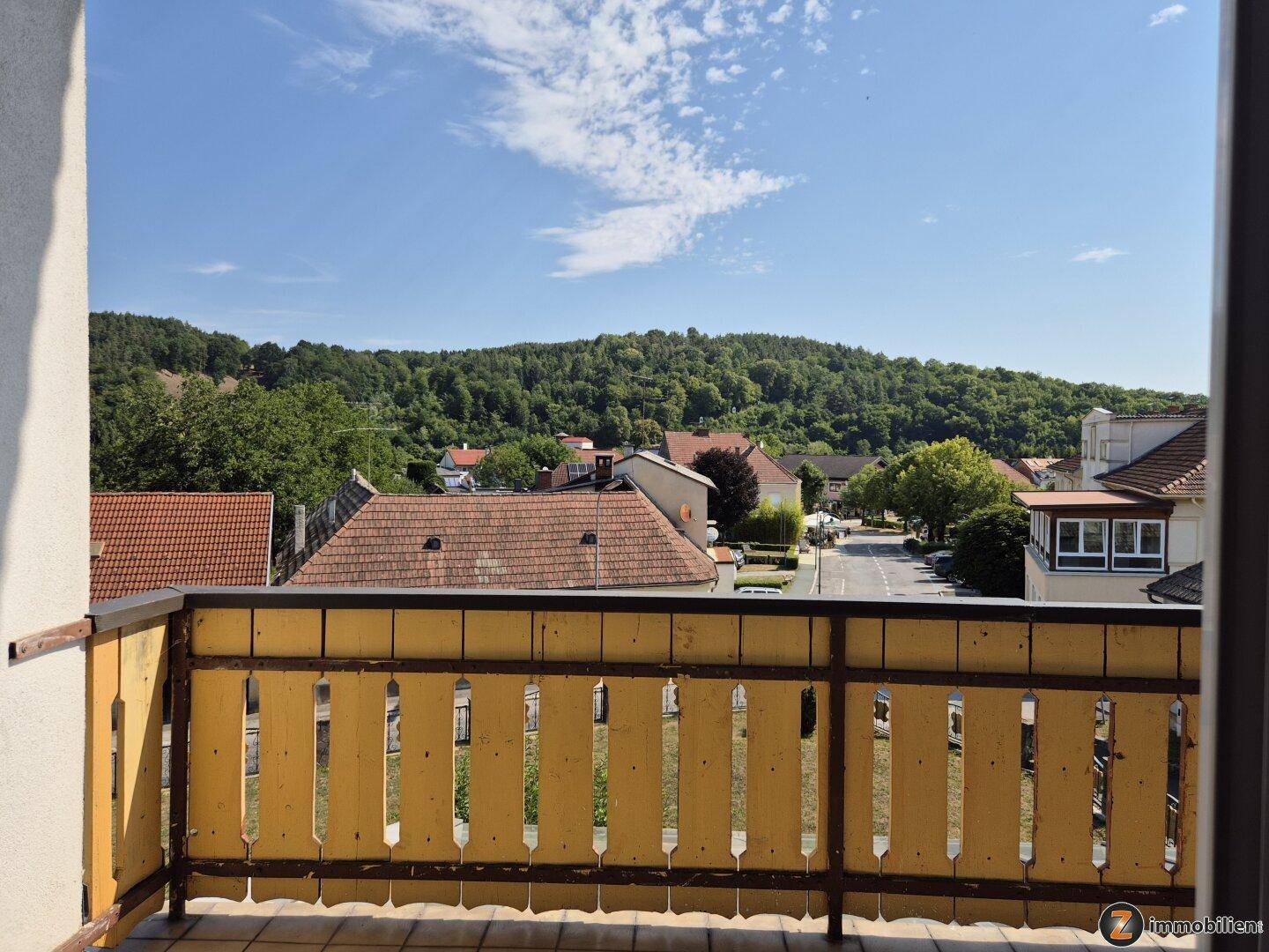 Balkon mit Holzgeländer und Panoramablick auf die umliegende Landschaft und den Ort.
