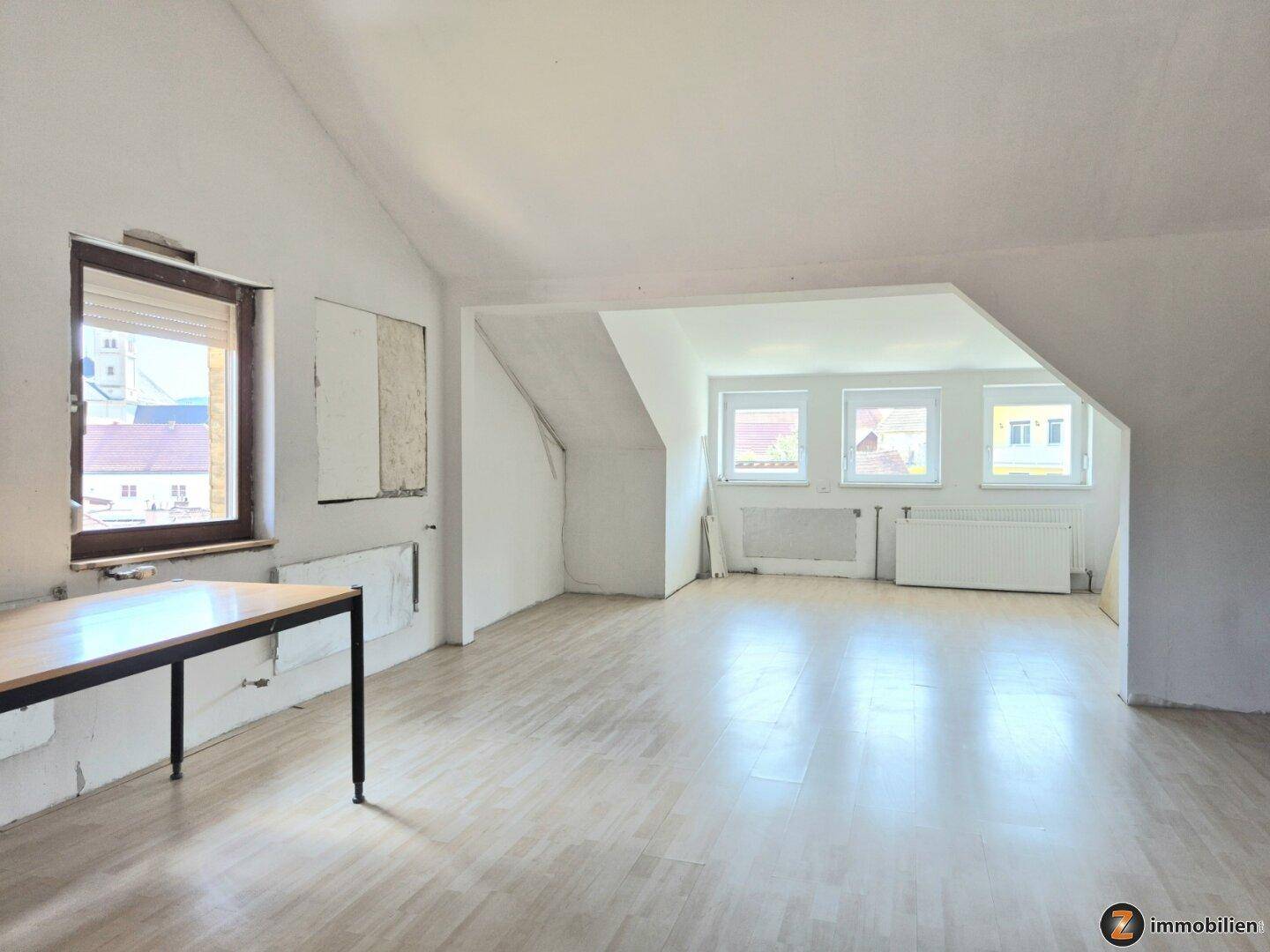 Großer offener Dachbodenraum mit Laminatboden, Schrägen und mehreren Fenstern.