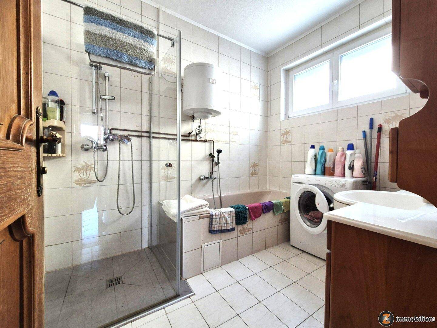 Badezimmer mit Dusche, Badewanne, Waschmaschine und Fenster in hellem Design.