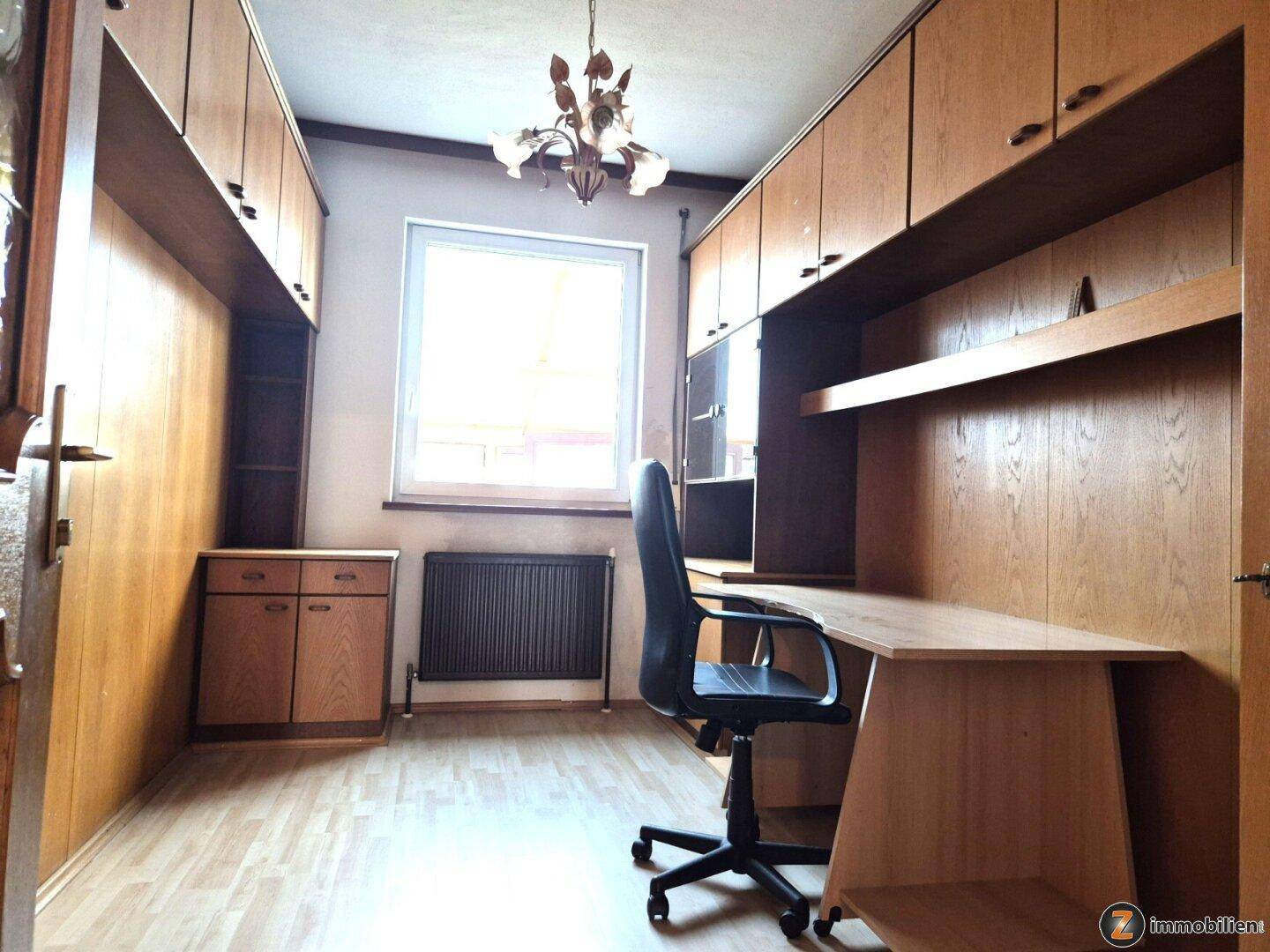 Arbeitszimmer mit Einbauschränken, Schreibtisch und Laminatboden.