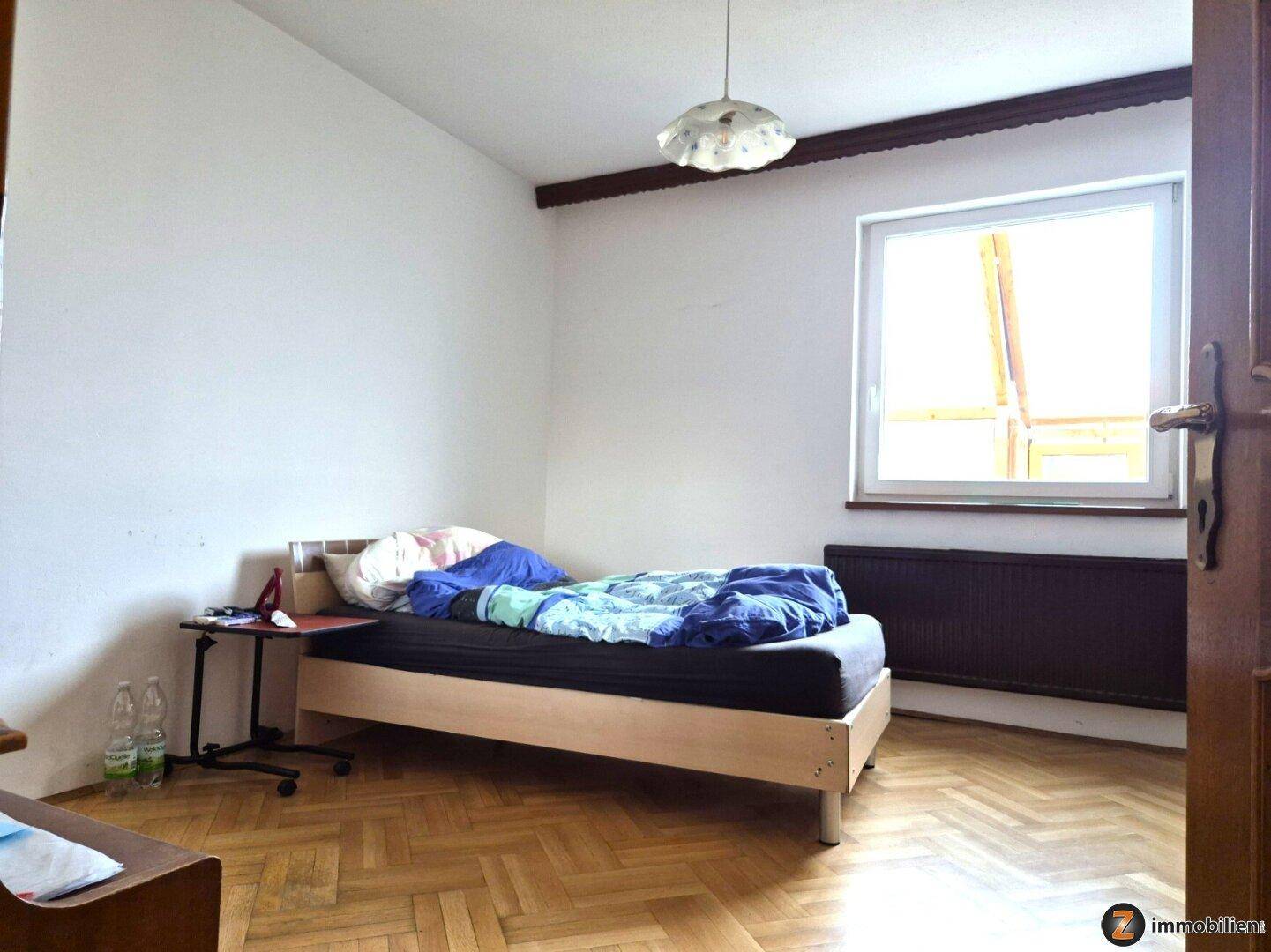 Schlafzimmer mit Einzelbett, Laminatboden und einem Fenster für natürliches Licht.