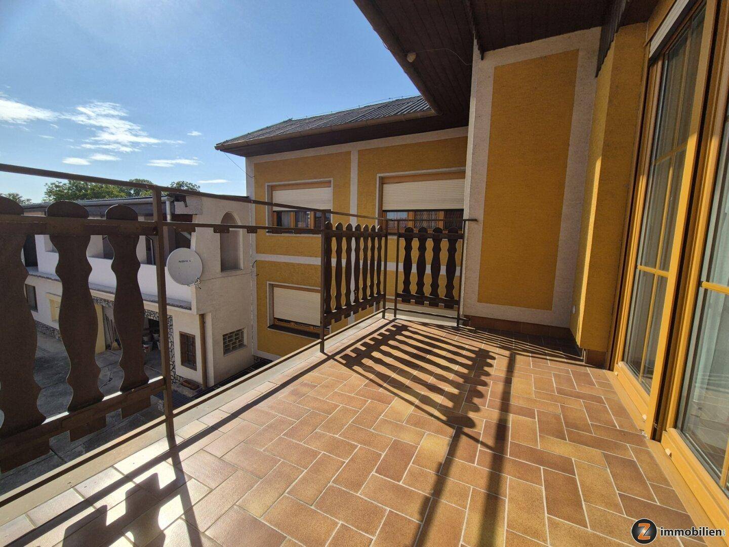 Geräumiger Balkon mit Terrakotta-Fliesen, traditionellem Holzgeländer und Blick auf die Umgebung.