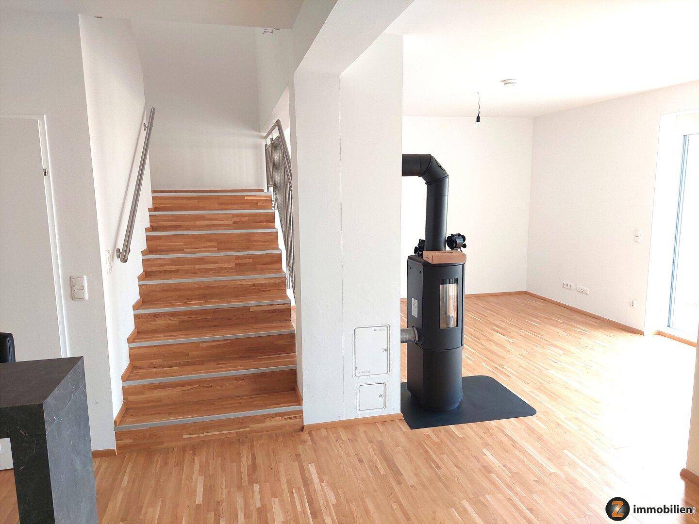 Heller Eingangsbereich mit Holztreppe und modernem Geländer, angrenzend an den Wohnbereich.