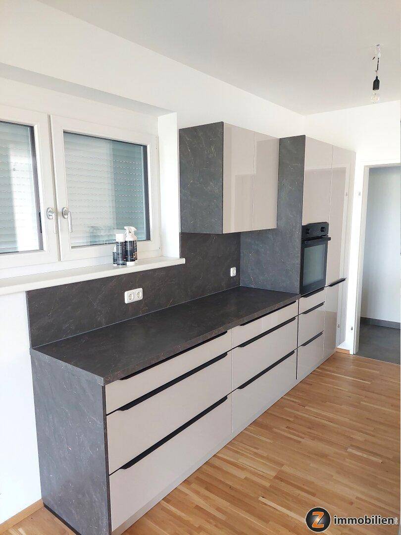 Moderne Einbauküche mit grauen Arbeitsplatten, hellen Schränken und integriertem Backofen.