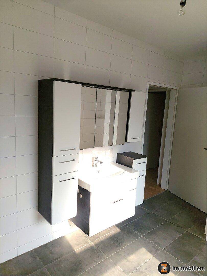 Modernes Badezimmer mit Waschtischunterschrank, Spiegelschrank und weißen Wandfliesen.