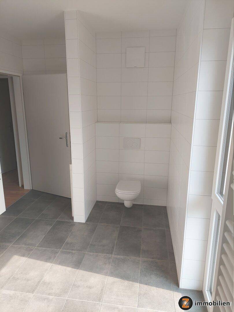 Separates WC mit wandhängender Toilette und modernen Fliesen an Wänden und Boden.