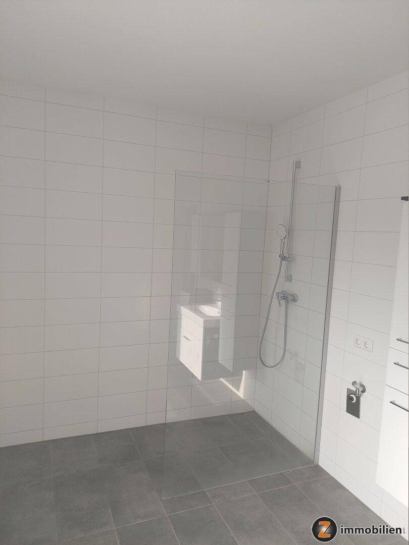 Helles Badezimmer mit ebenerdiger Dusche und modernen Fliesen in Weiß und Grau.