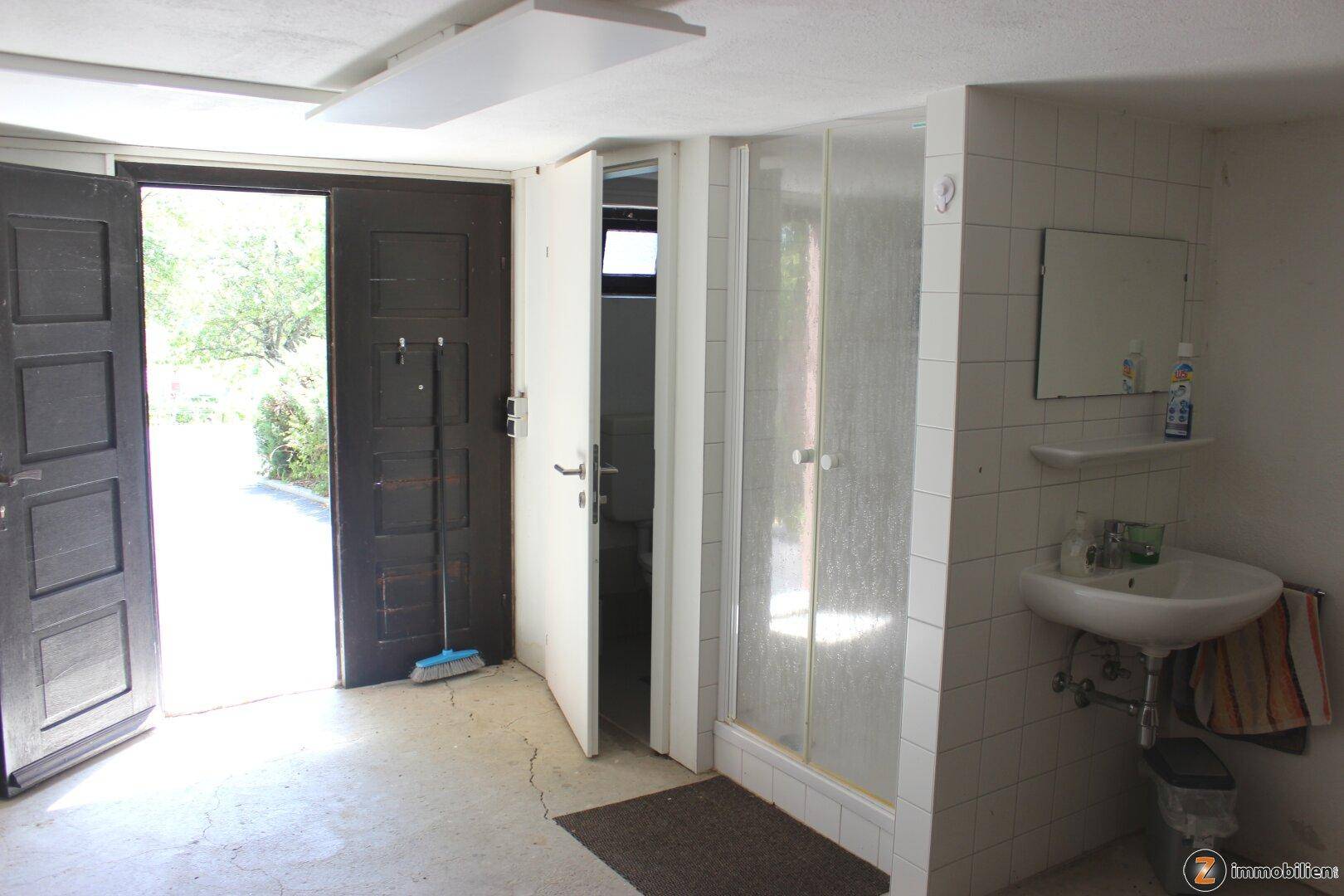 Einfaches Badezimmer mit Dusche, Waschbecken und direktem Zugang zum Gartenbereich.