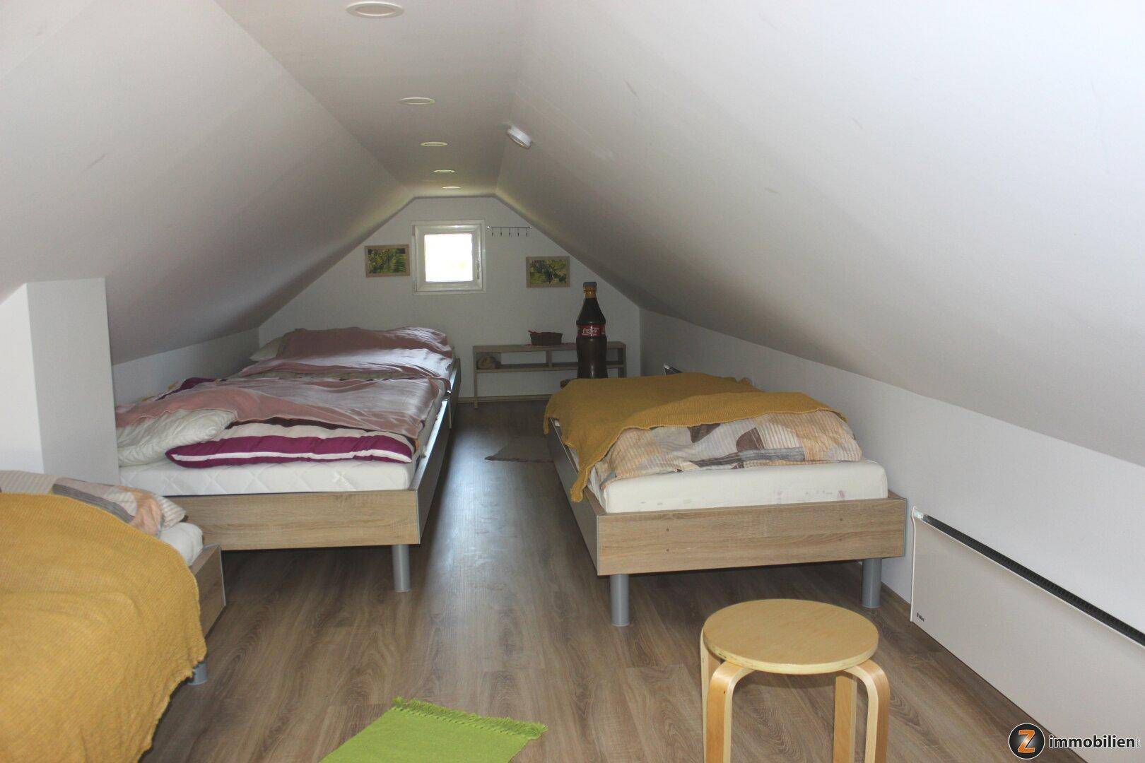 Dachgeschosszimmer mit mehreren Schlafplätzen, Laminatboden und kleinem Fenster für natürliches Licht.