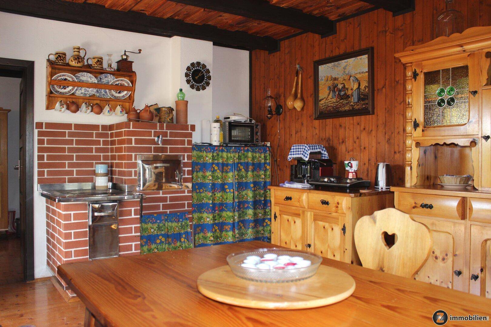Rustikale Wohnküche mit Holzwänden, gemauertem Ofen und traditionellen Holzmöbeln.