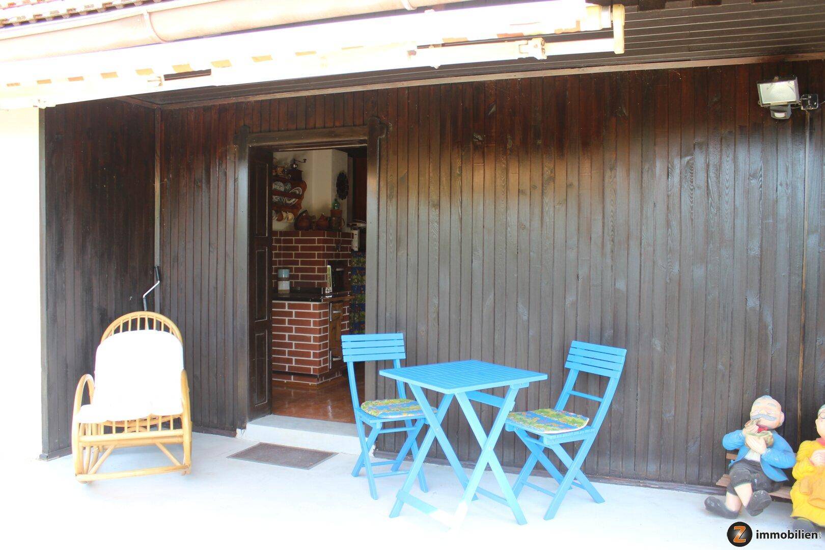 Überdachte Terrasse mit blauen Gartenmöbeln und direktem Zugang zur Küche des Hauses.