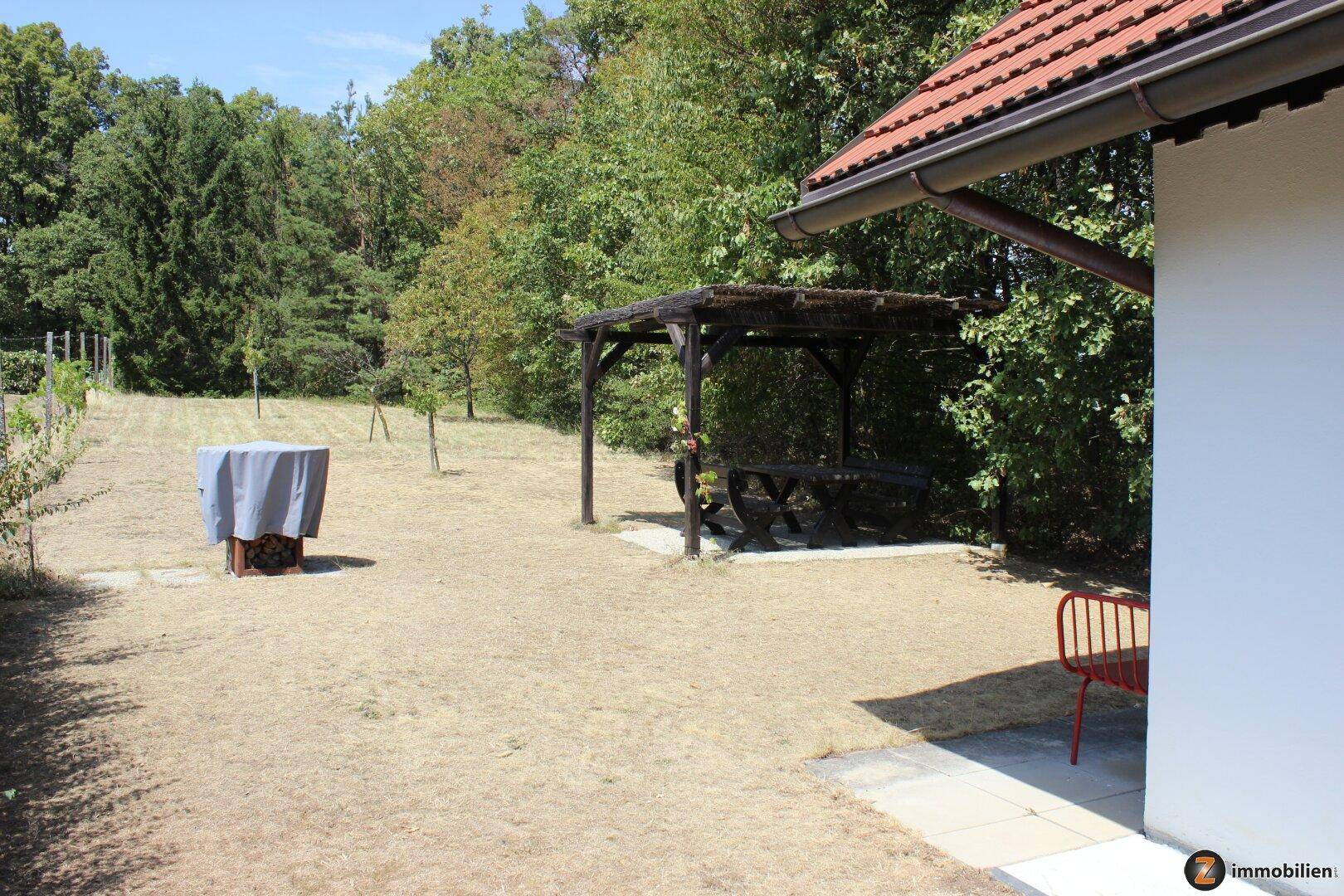 Weitläufiger Gartenbereich mit Rasenfläche, Bäumen und einer Holzpergola im Hintergrund.