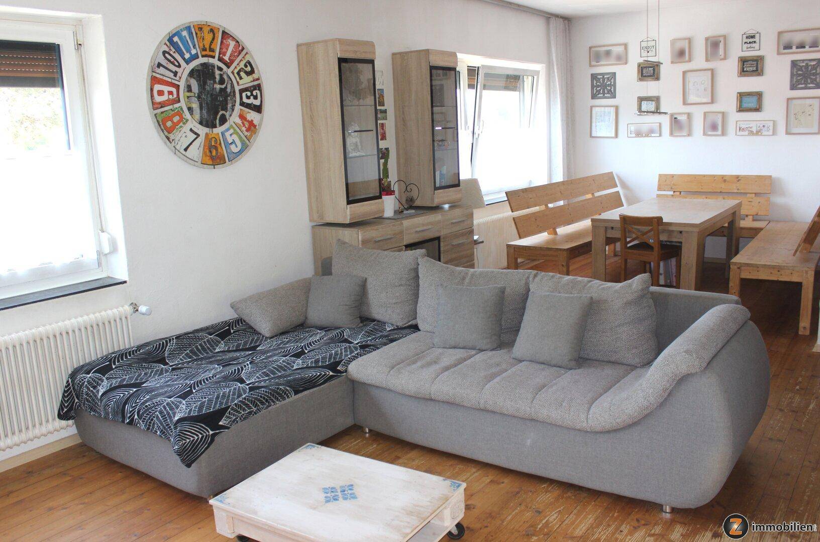 Gemütlicher Wohn-Essbereich mit grauem Ecksofa, Holzboden und rustikalen Holzmöbeln.