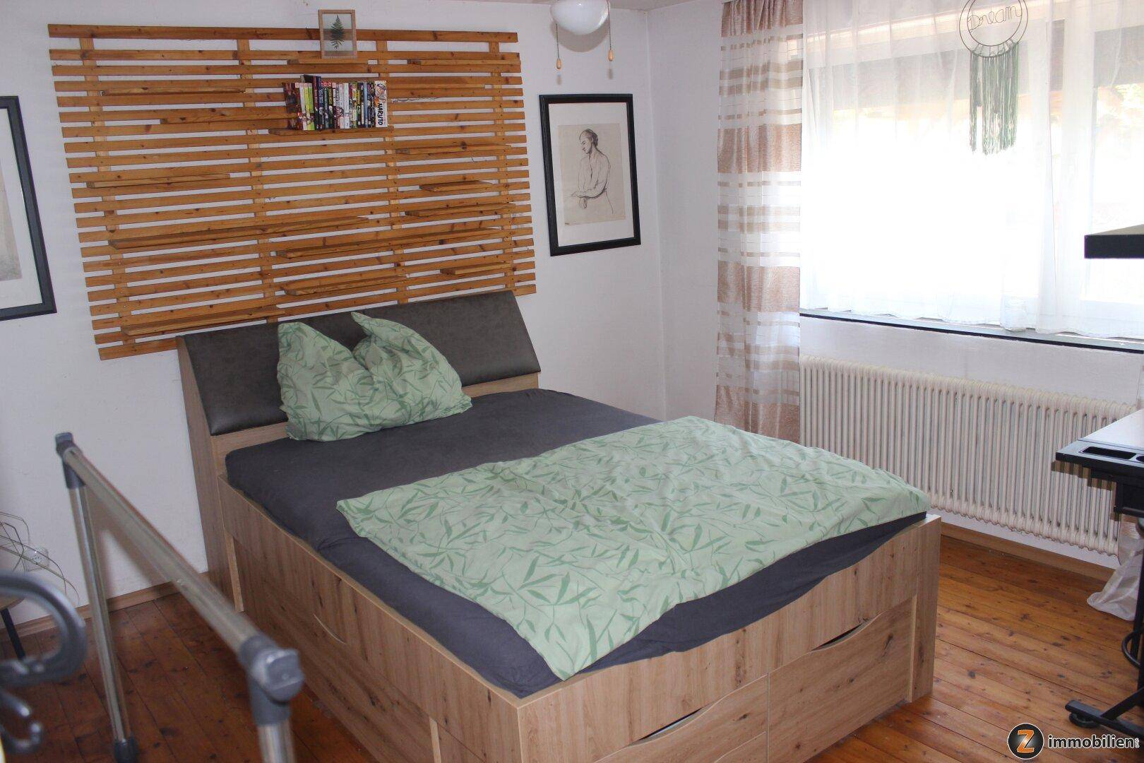 Schlafzimmer mit Holzbett, grüner Bettwäsche und Holzboden, hell durch großes Fenster.