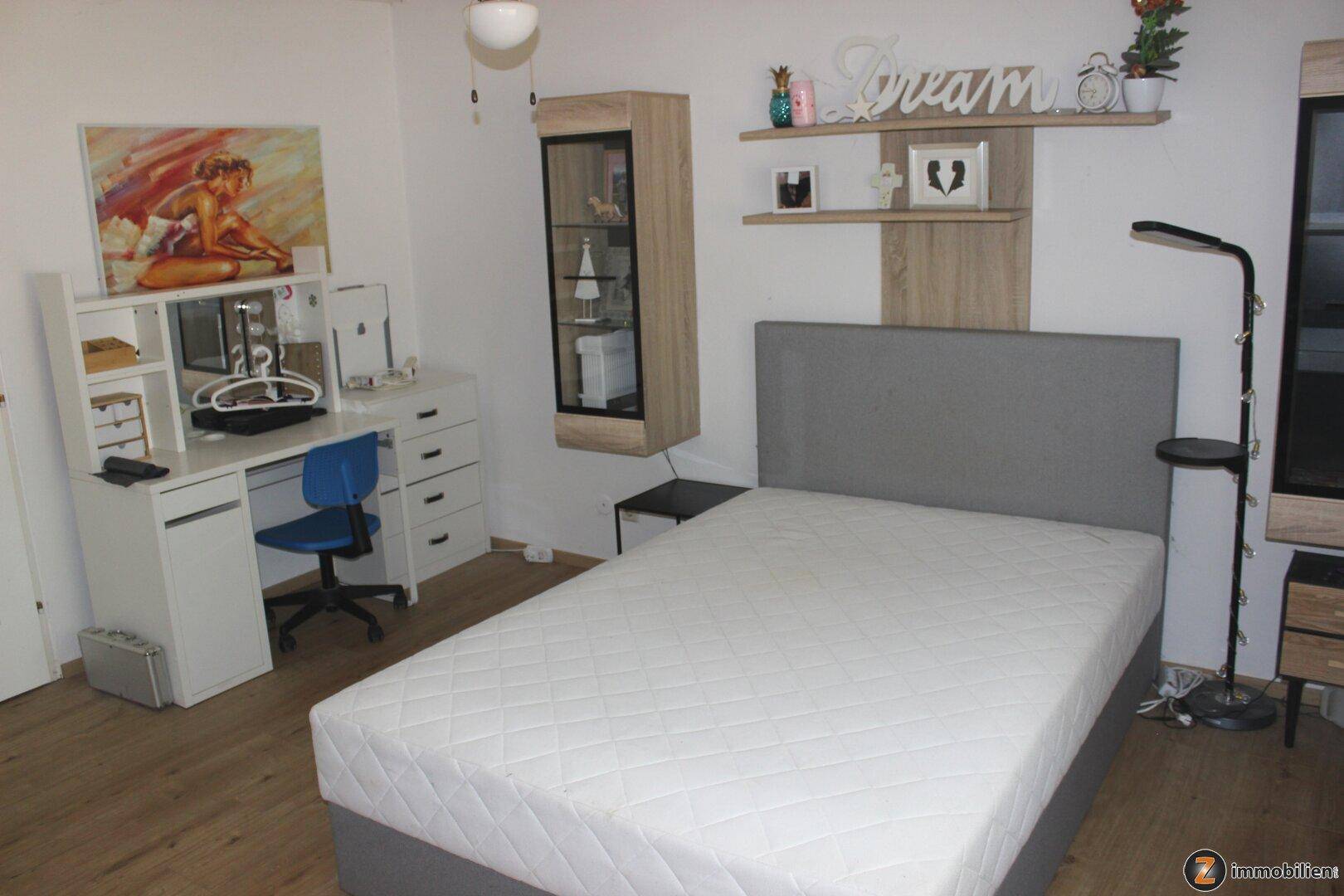 Helles Schlafzimmer mit Bett, weißem Schreibtisch und modernen Wandregalen.