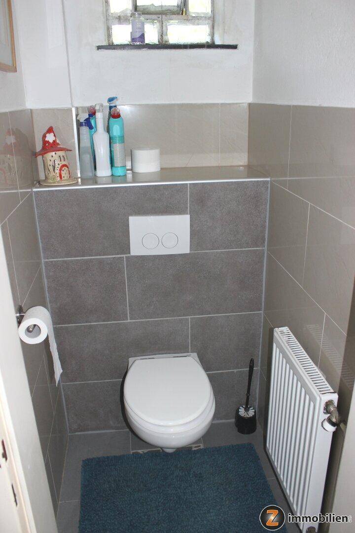 Separates WC mit wandhängender Toilette, kleinem Fenster und modernen Fliesen.