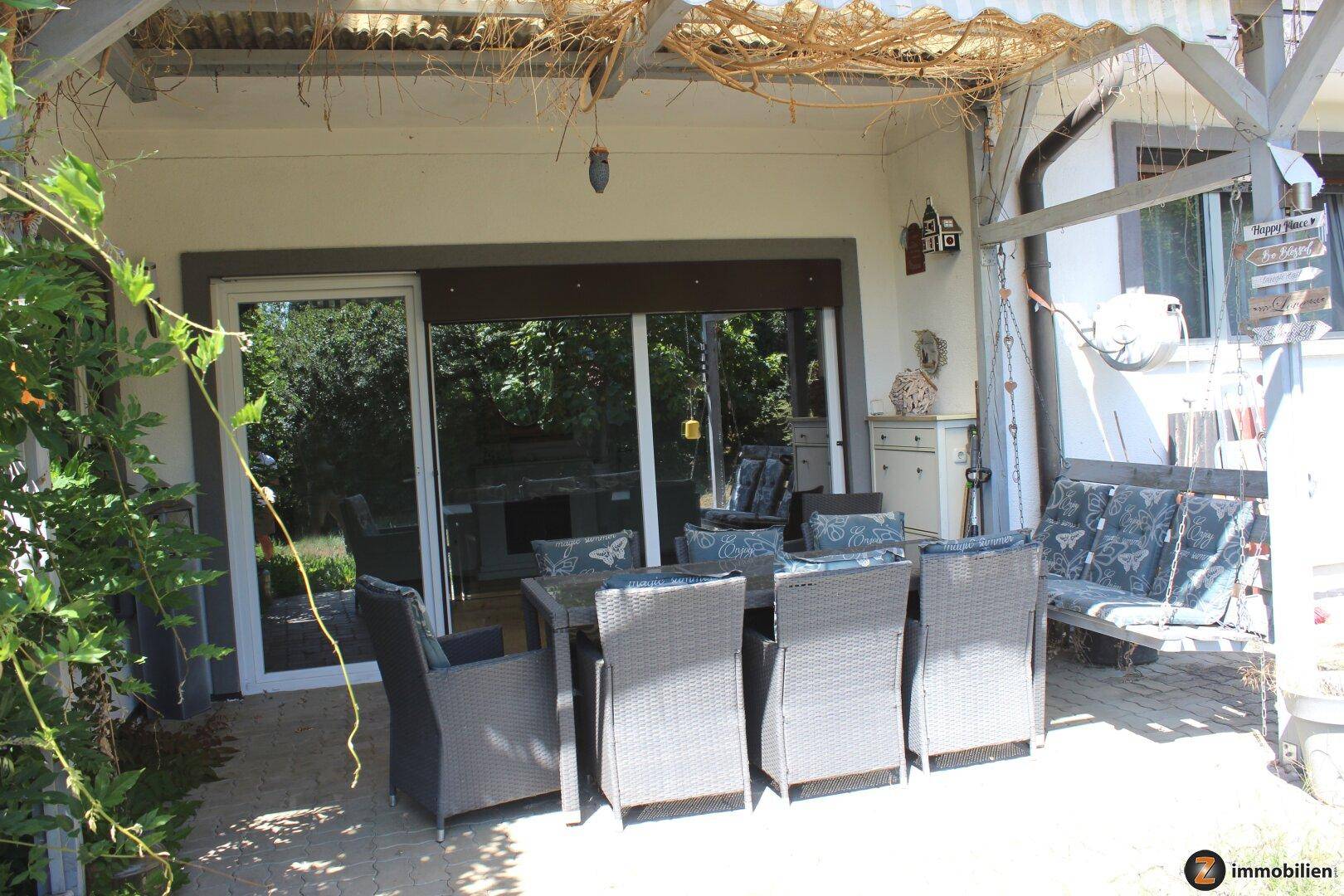 Überdachte Terrasse mit Esstisch und Schaukelbank, ideal für entspannte Stunden im Freien.