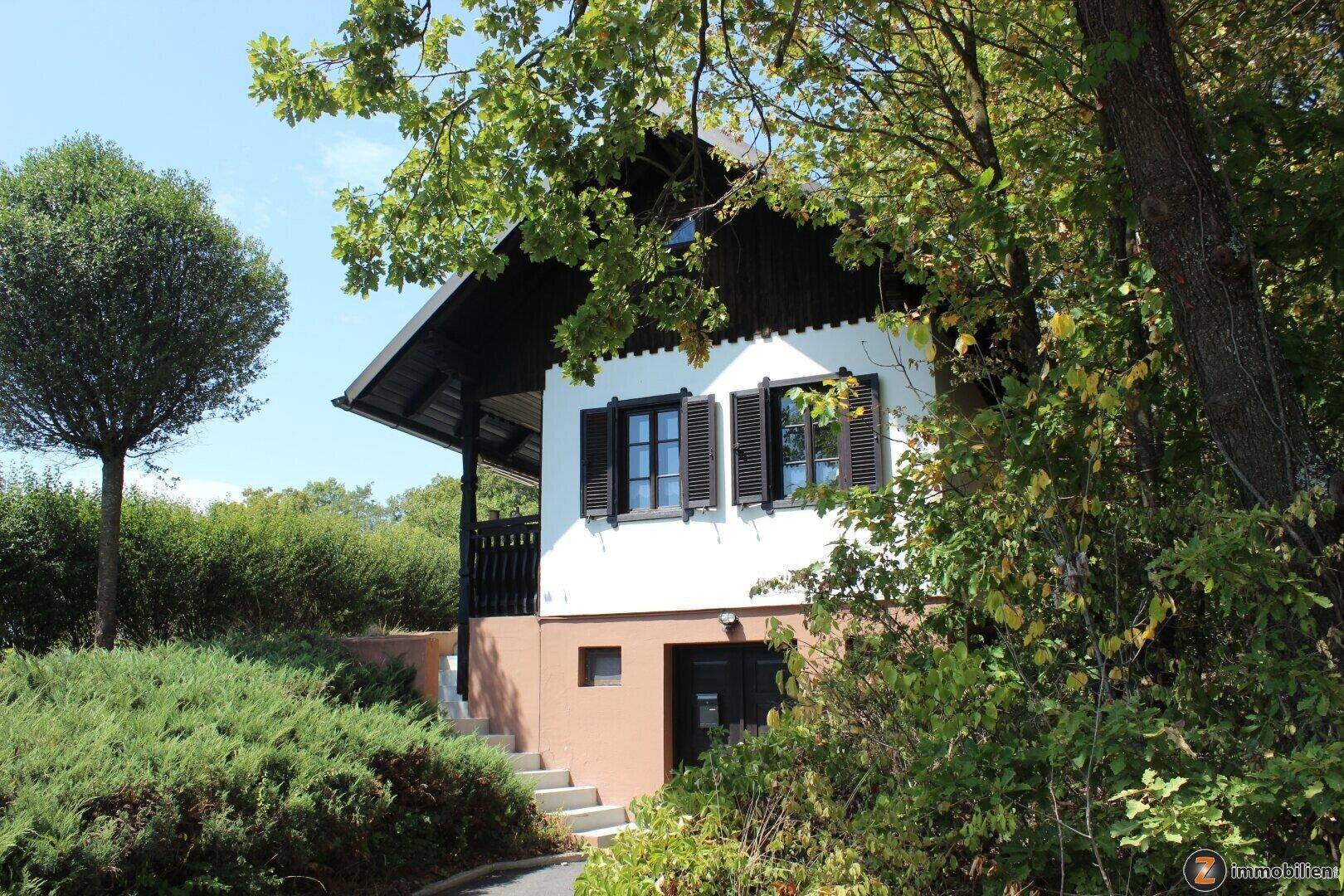 Vorderansicht des Hauses mit dunklen Fensterläden und einem Eingangsbereich im Untergeschoss.