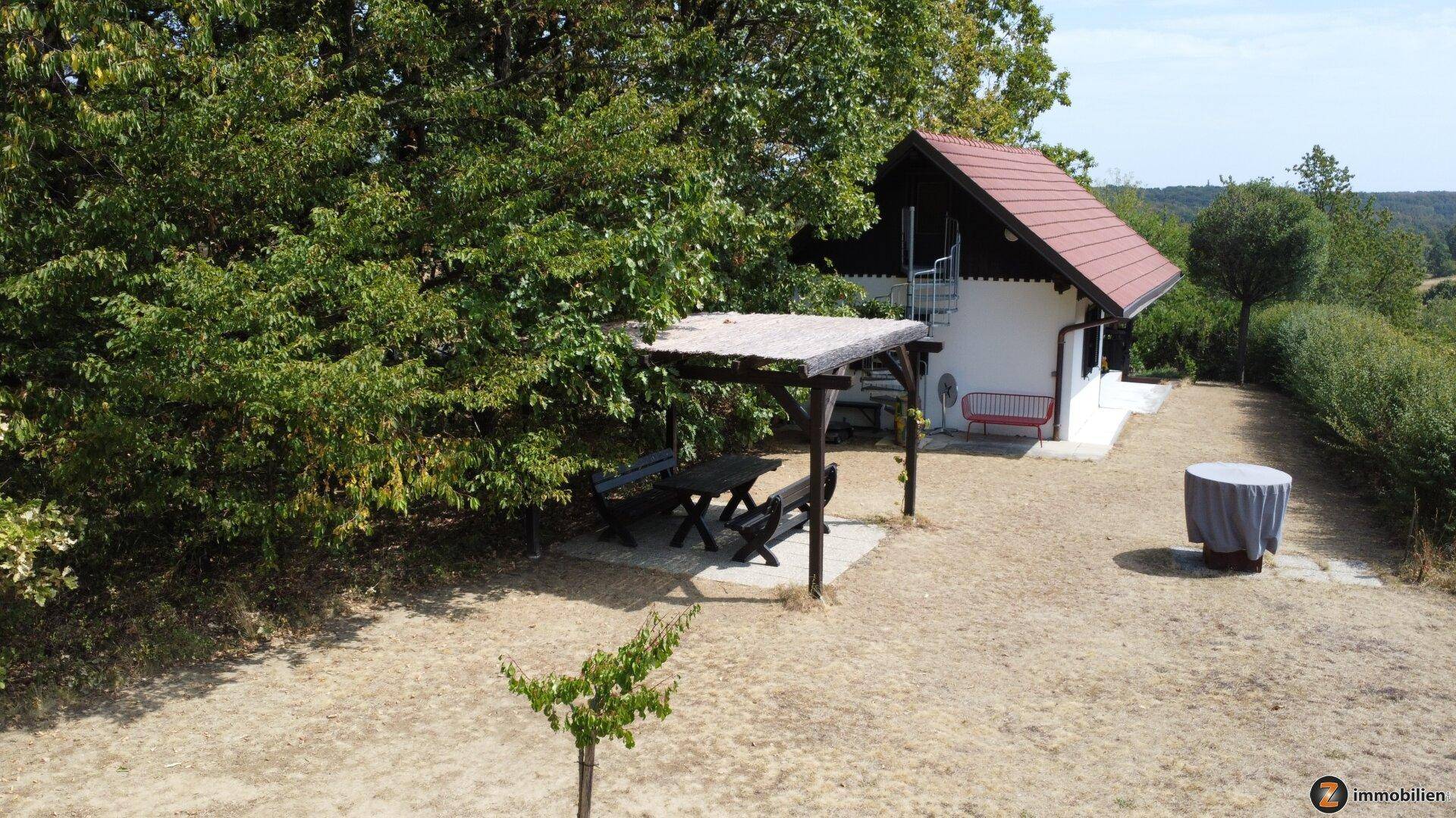 Gartenbereich mit überdachtem Sitzplatz und Blick auf das kleine Haus im Grünen.