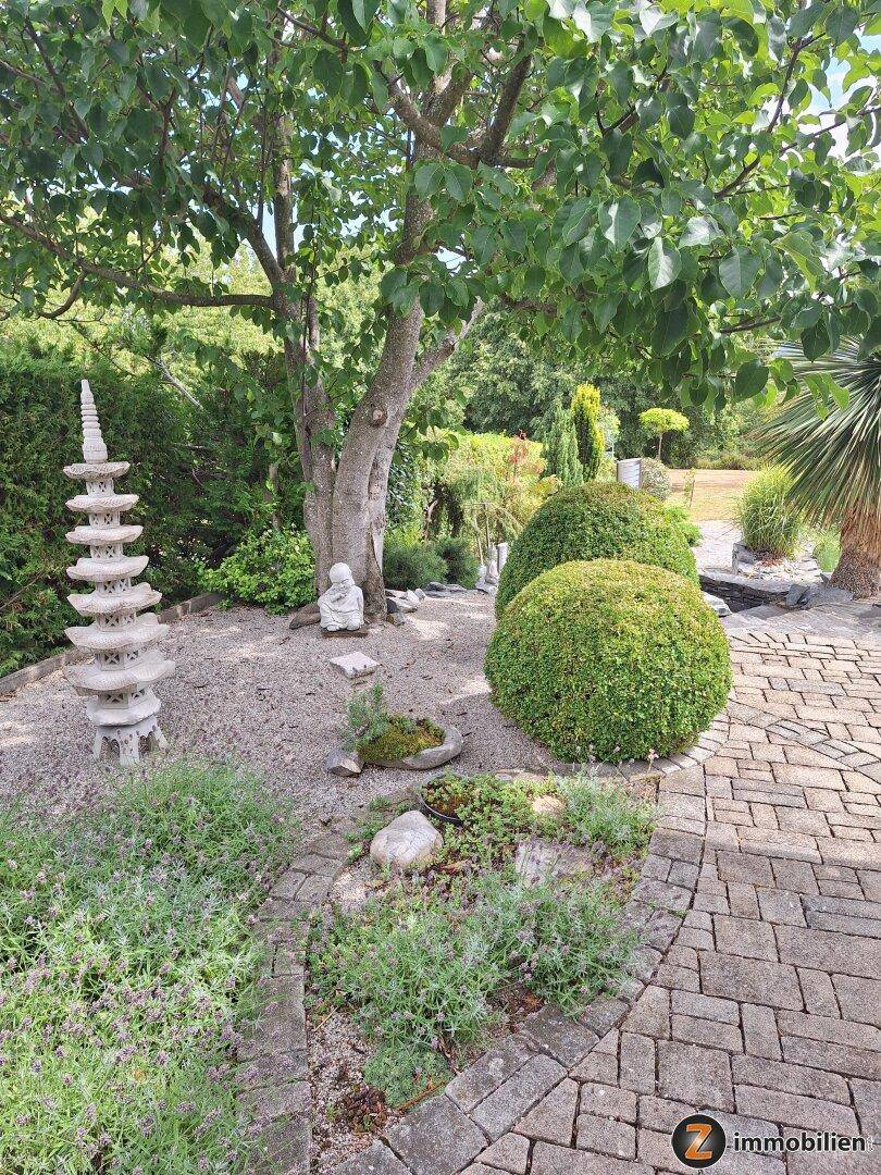 Asiatisch inspirierter Gartenbereich mit Steinpagode, Buddha-Statue und Kieswegen.