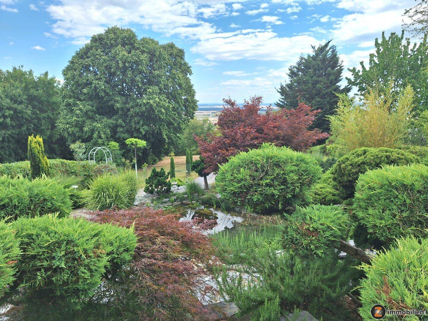 Gepflegter Garten mit üppiger Vegetation, einem kleinen Teich und weitem Blick in die Landschaft.