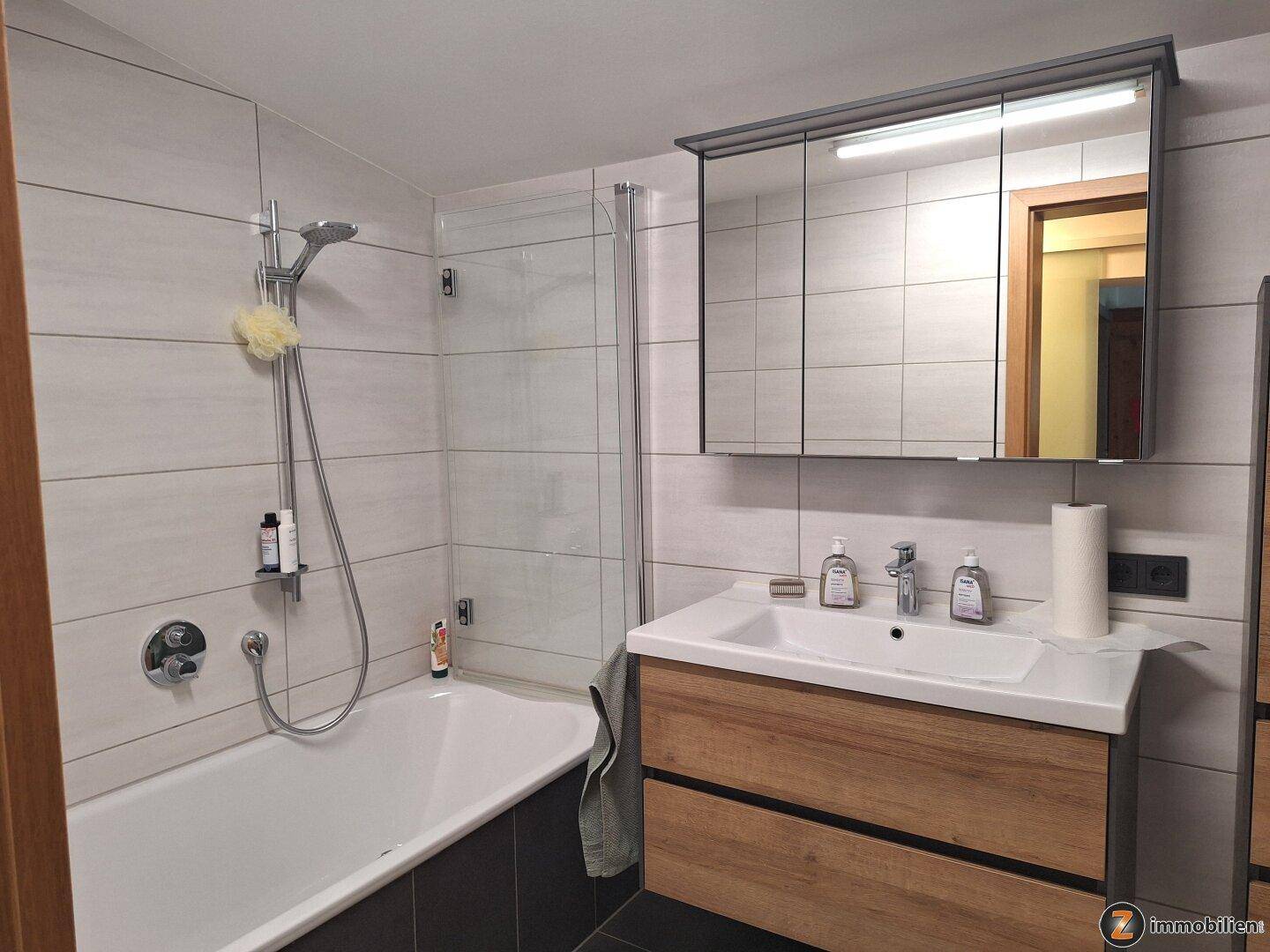 Modernes Badezimmer mit Badewanne, Duschfunktion, Waschbecken und Spiegelschrank.