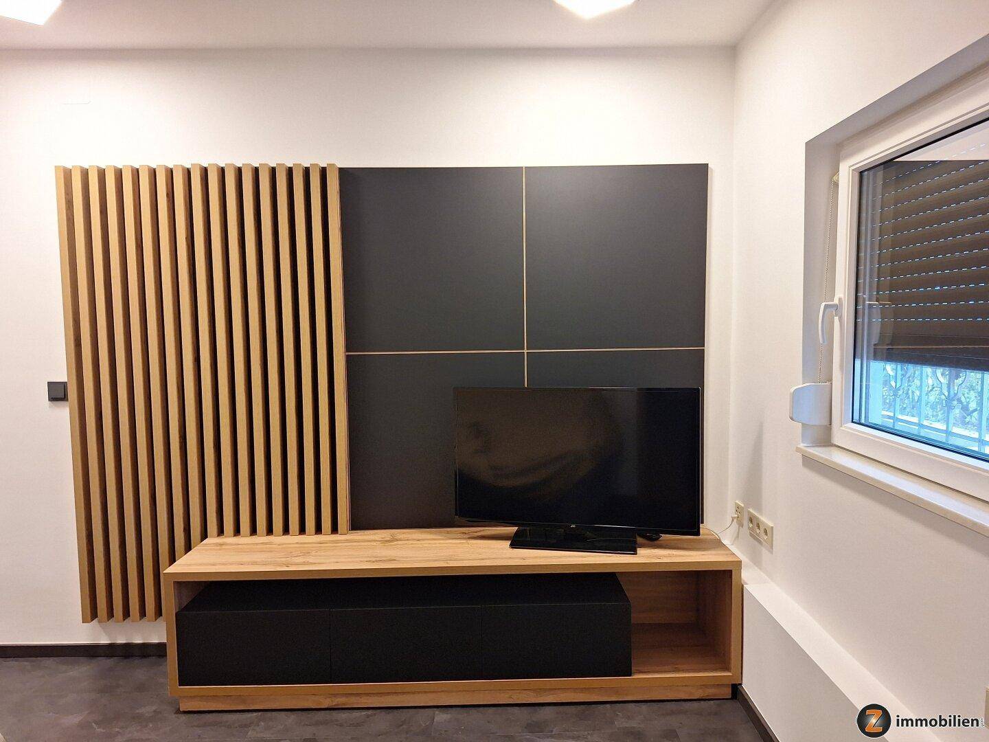 Moderner Wohnbereich mit TV-Möbeln, Holzlamellenwand und Fenster mit Rollladen.