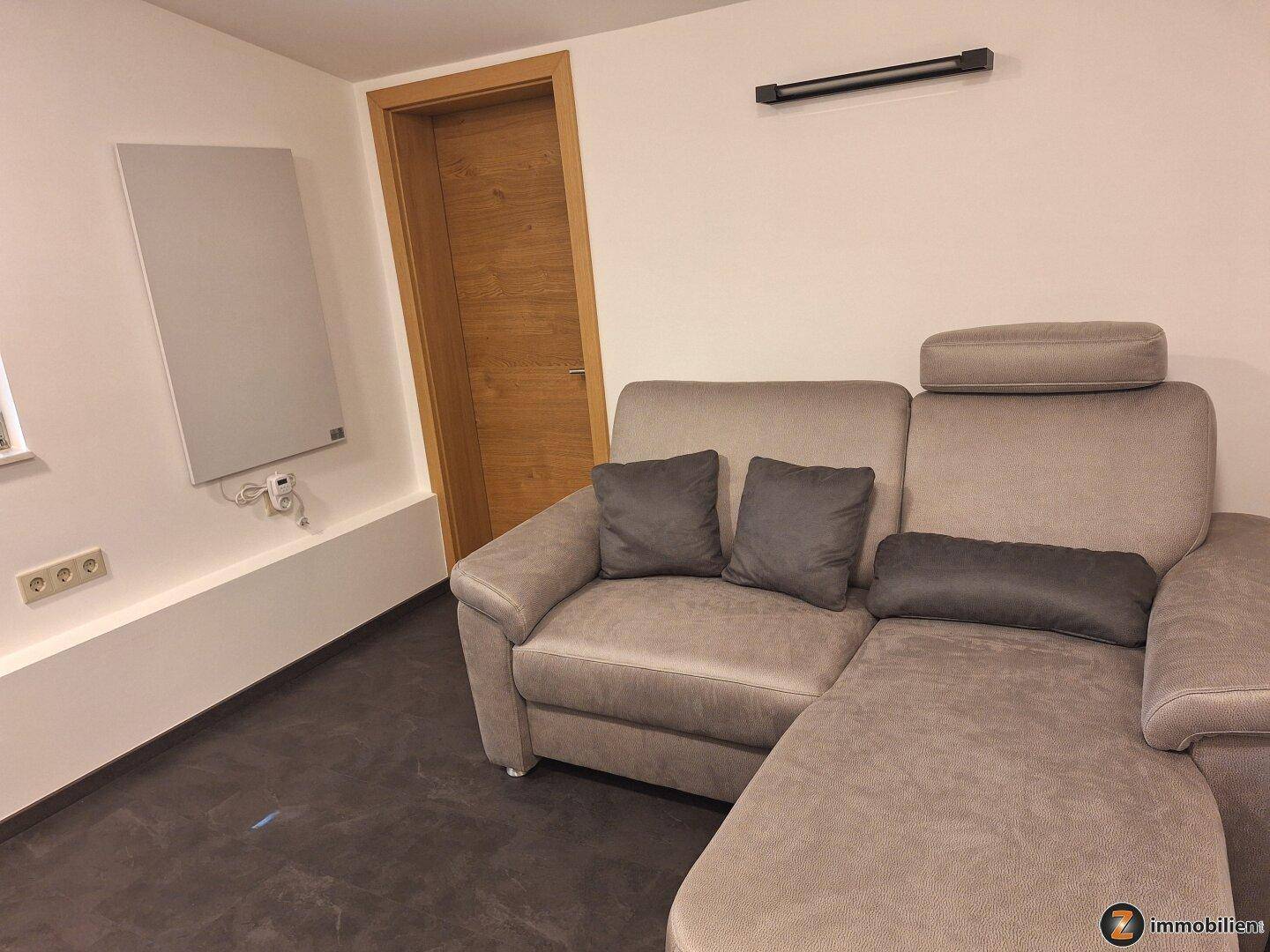 Gemütlicher Wohnbereich mit Ecksofa und moderner Infrarotheizung an der Wand.