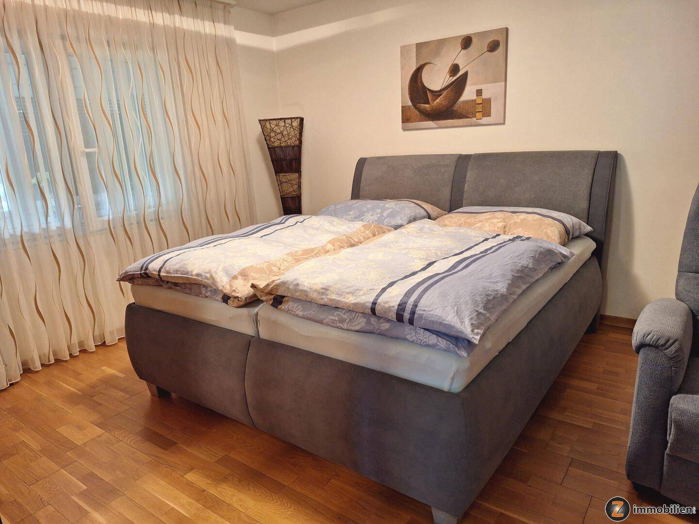 Schlafzimmer mit Doppelbett, Holzboden und Vorhängen, die für eine gemütliche Atmosphäre sorgen.