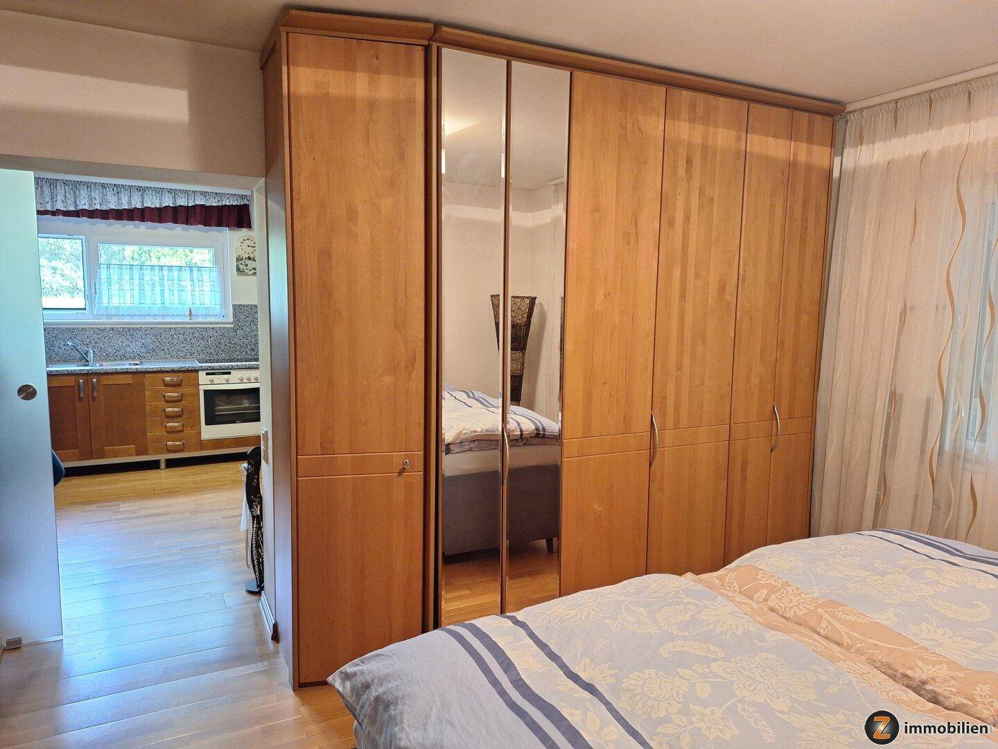 Schlafzimmer mit großem Spiegelschrank und Blick in die angrenzende Küche.