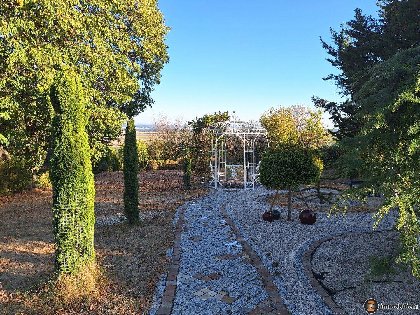 Romantischer Gartenweg führt zu einem weißen Pavillon mit Sitzgelegenheiten und weitem Blick.